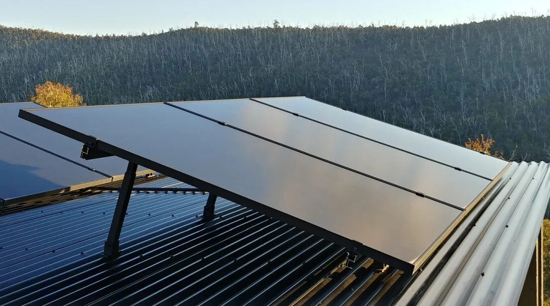 Some Hyundai solar panels installed on a metal roof with a forested landscape in the background.