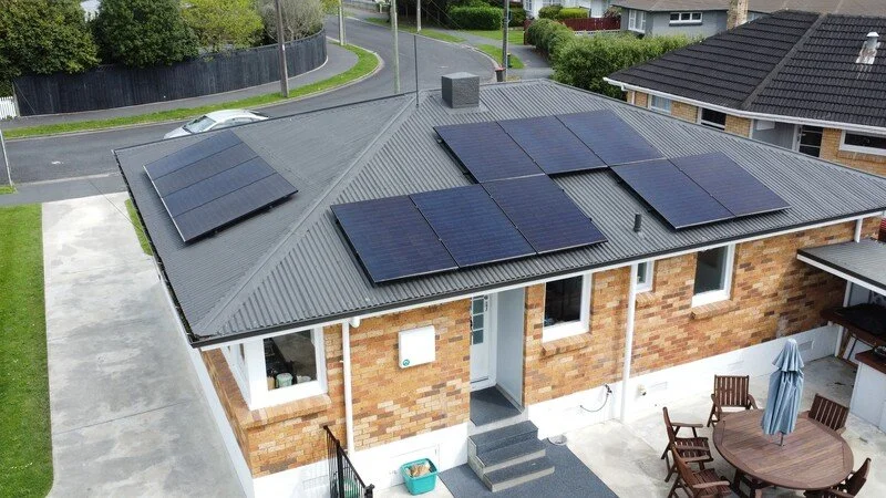 Aerial view of a brick house with a metal roof equipped with 12 modern, all-black solar panels.
