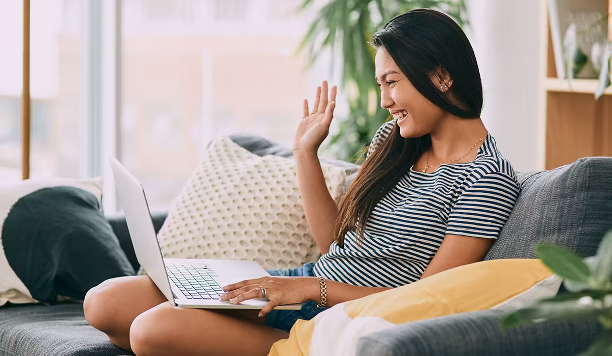 A woman sitting on a gray sofa having a solar design consultation on your laptop looking happy and enjoying the process