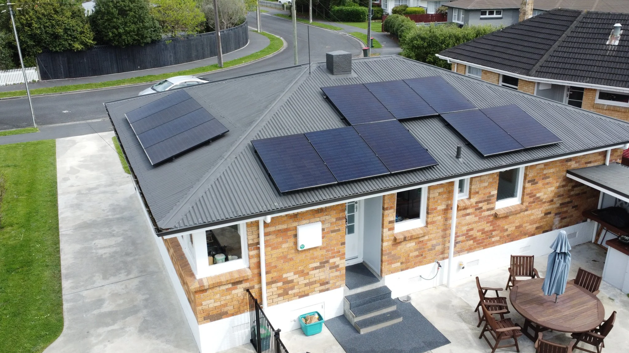Aerial view of a brick house with a metal roof equipped with 12 modern, all-black solar panels.