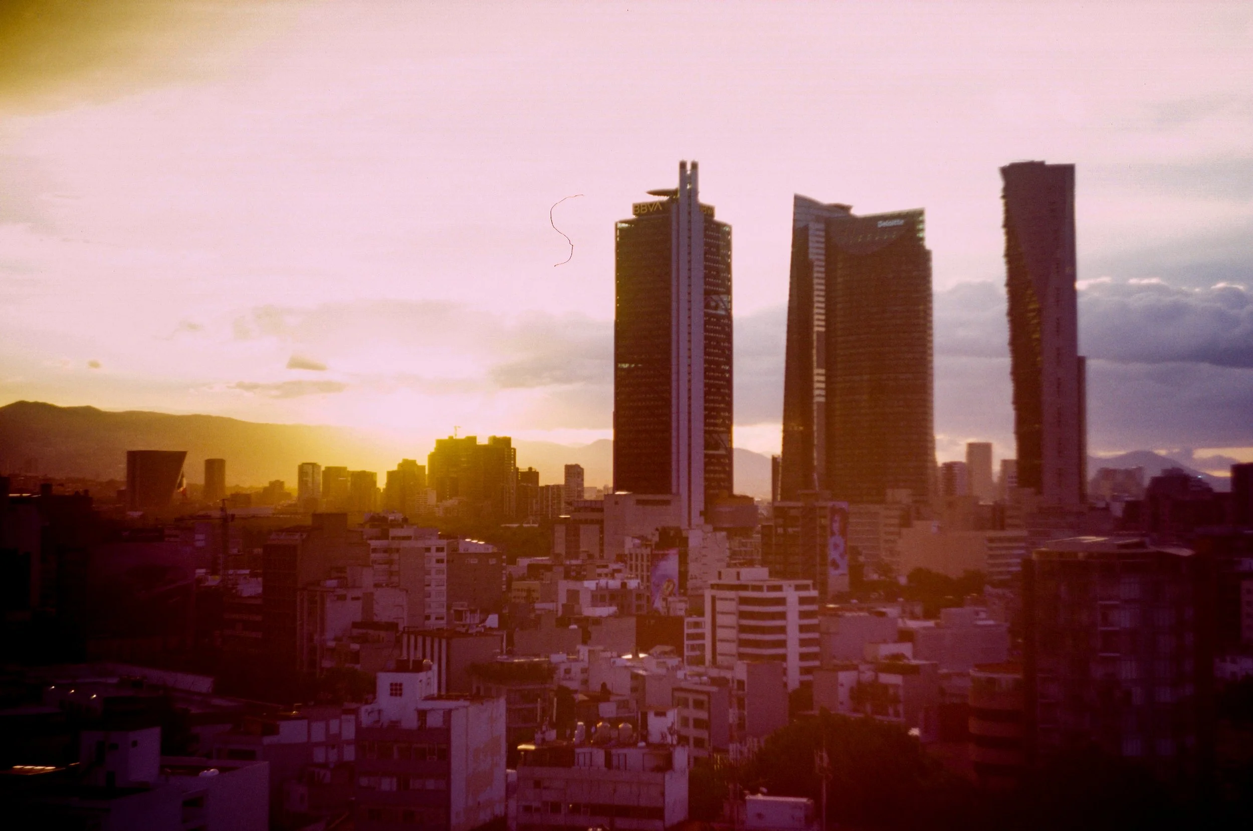 City skyline at sunset with tall skyscrapers and mountain range in the background - Shot on 35mm film