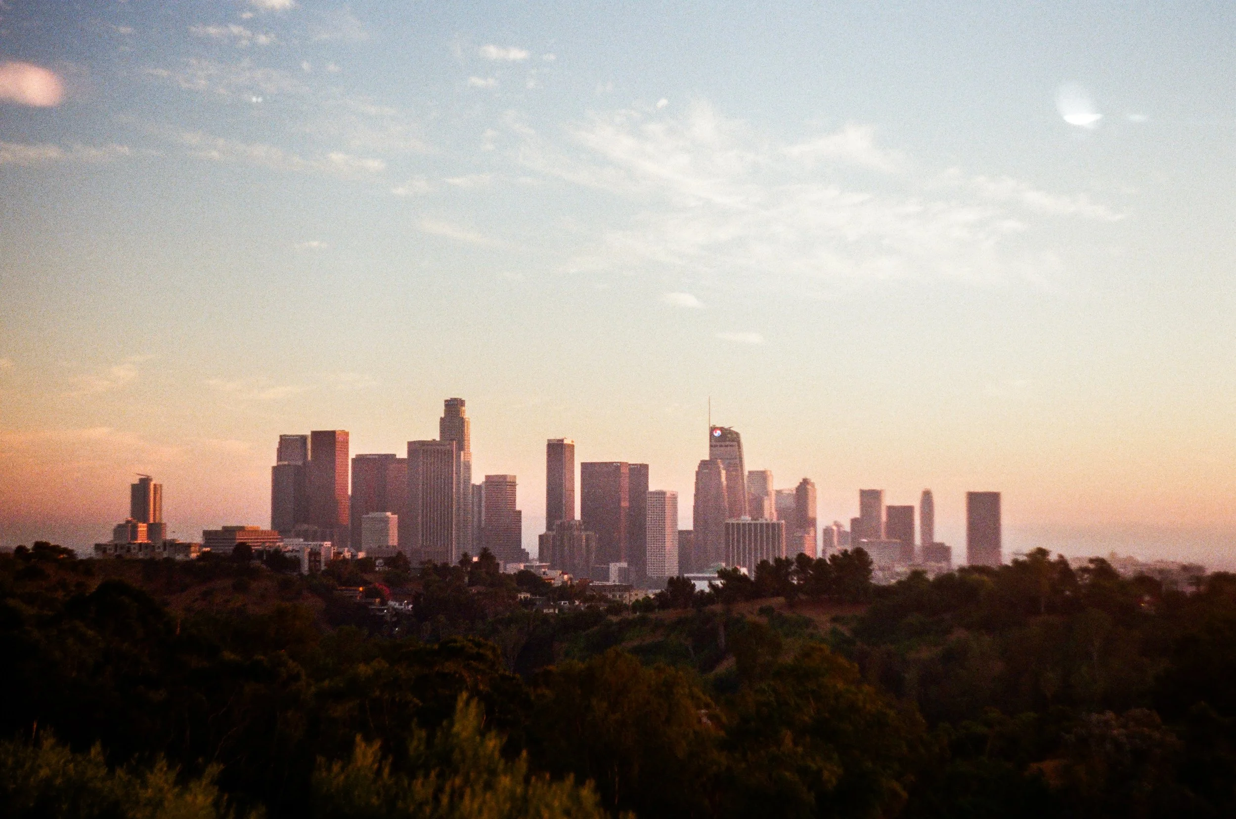 City skyline at sunset with skyscrapers and trees in the foreground.