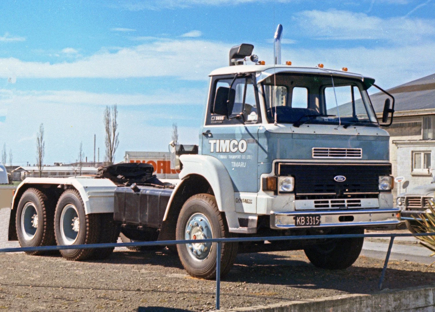 Vintage blue and white Ford truck on display outdoors, labeled 'TIMCO' on the cab door, and a clear sky background.