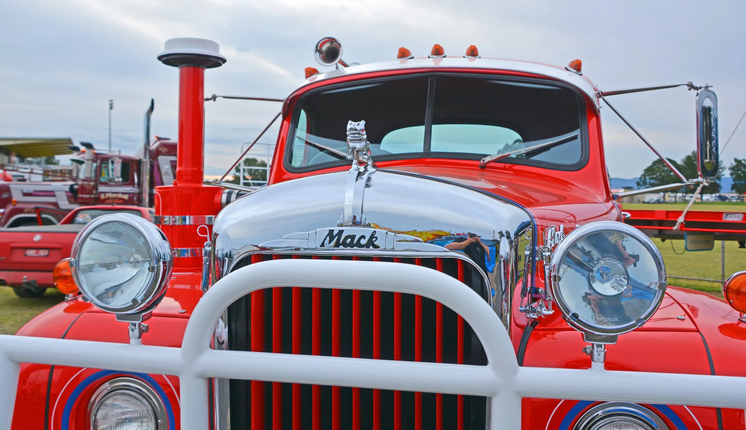 a red truck with a shiny grill siotting at a truck show with trucks in the background