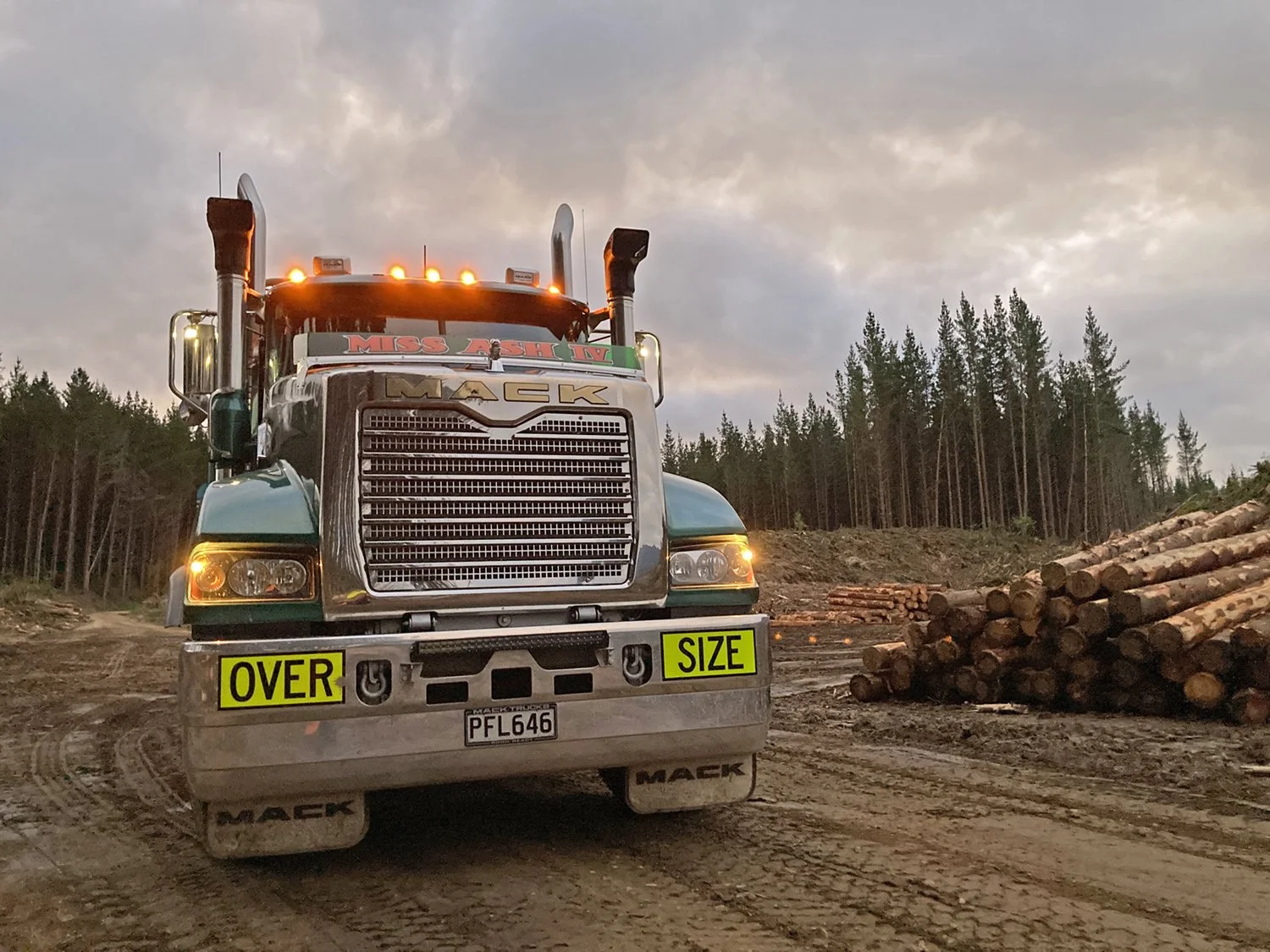A truck sitting on a forestry skid site with terr and logs in the background