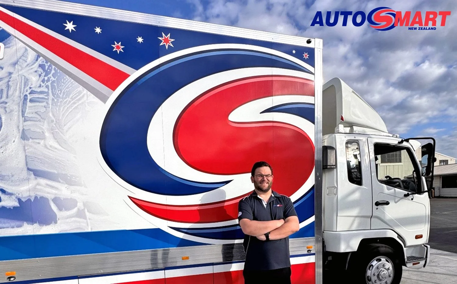 A man standing in front of  a brightly sign written, red white and blue box body truck