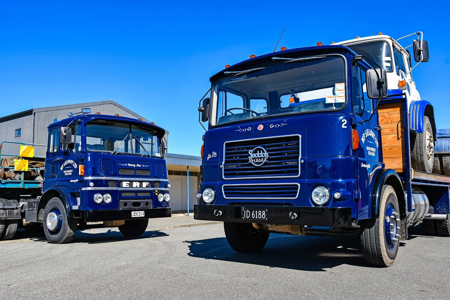 Two old restored build trucks sitting on a road with a building in the background