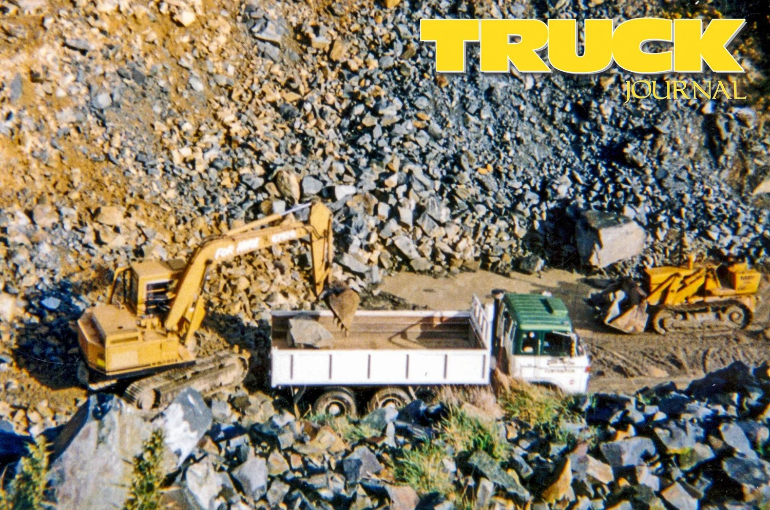 A truck being loaded in a quarry by and excavator with a bulldozer in the background