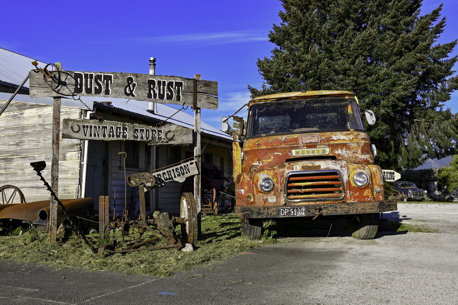 A rusty old truck parked beside a wooden buiding and some signs