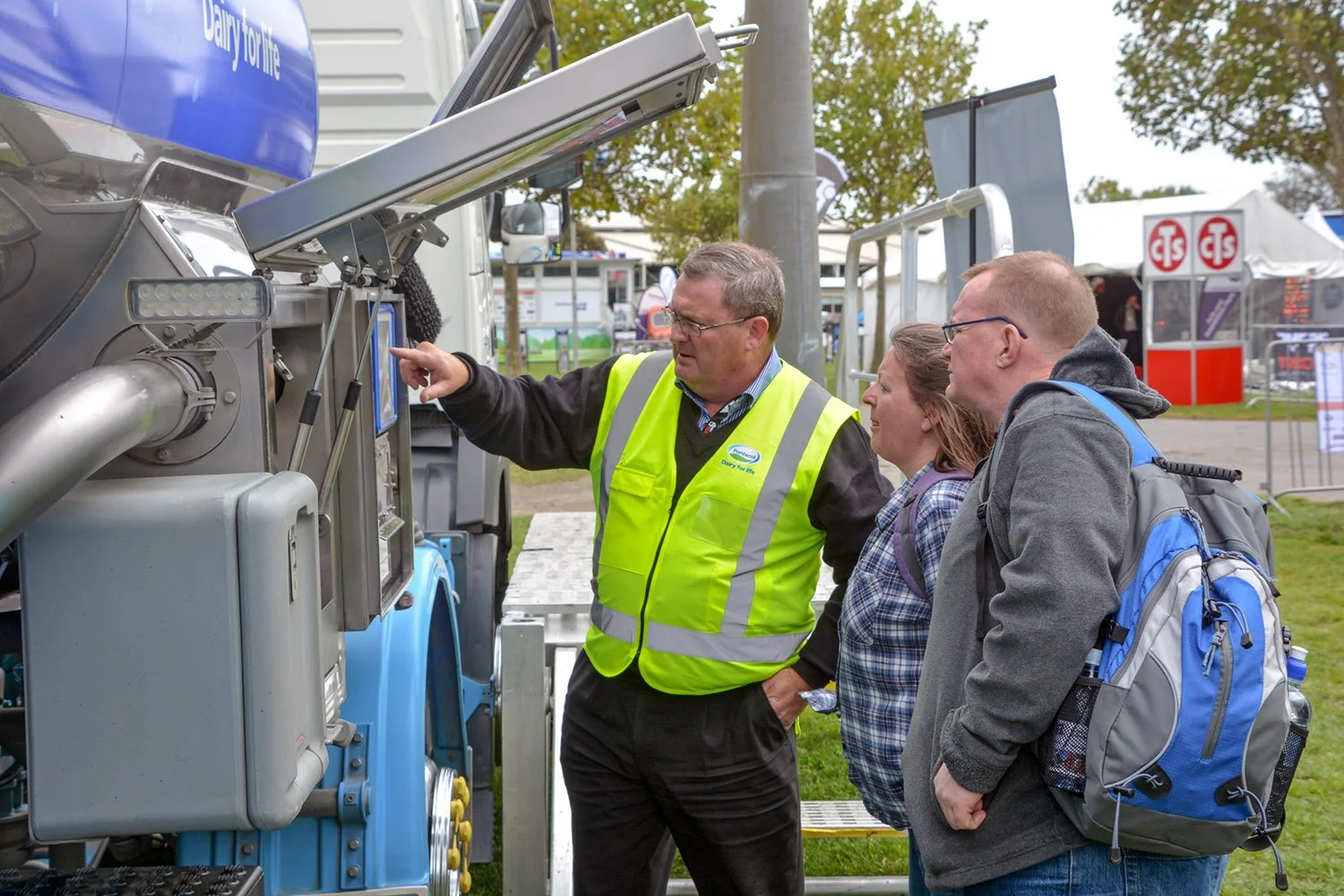 three people looking at a control unit in a cabinet on the side of a tanker truck