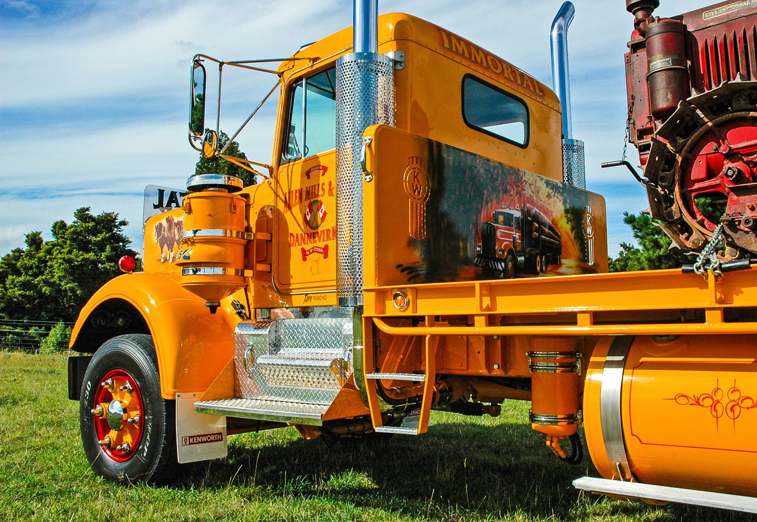A yellow flat deck truck with a bulldozer on its deck parked on grass
