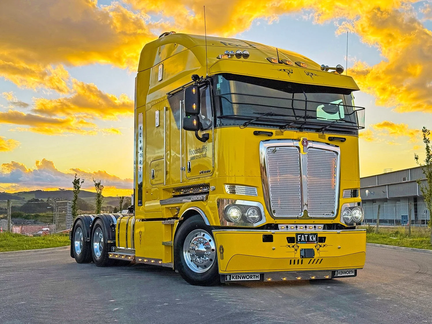 A yellow truck parked on the road with buildings and hills in the background