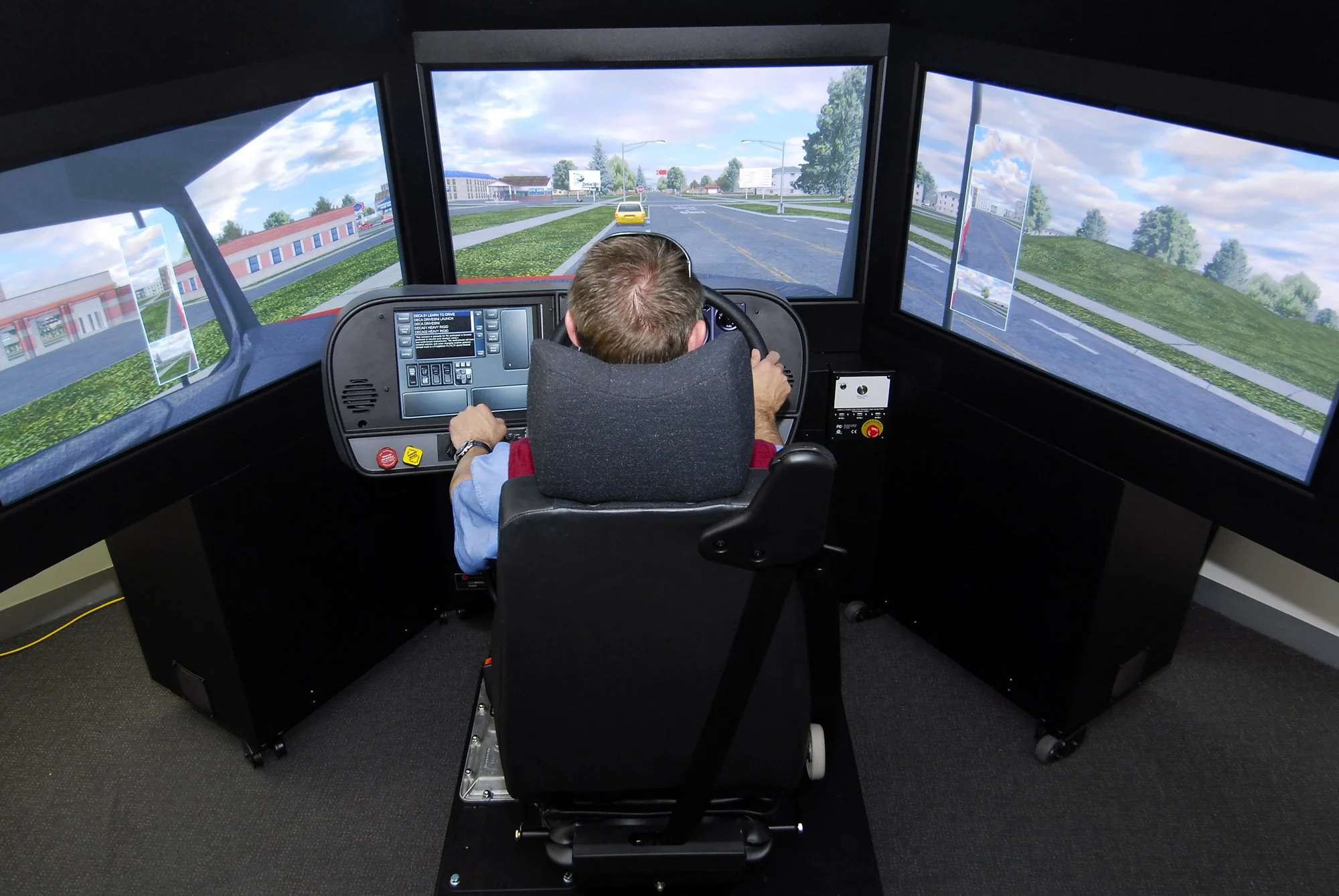 A person sitting in a truck simulator with three tv screens undergoing driver training