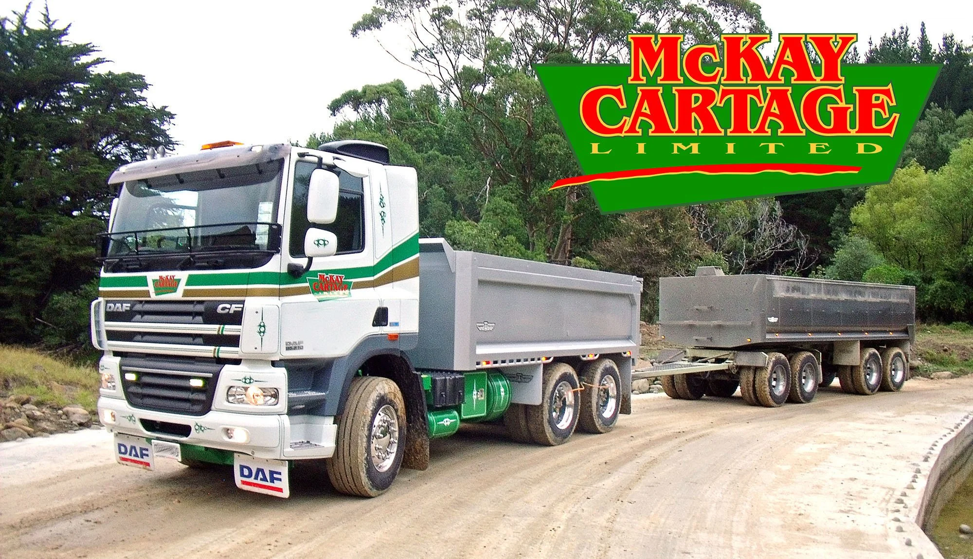 A white tip truck and trailer on a shingle road with trees in the background