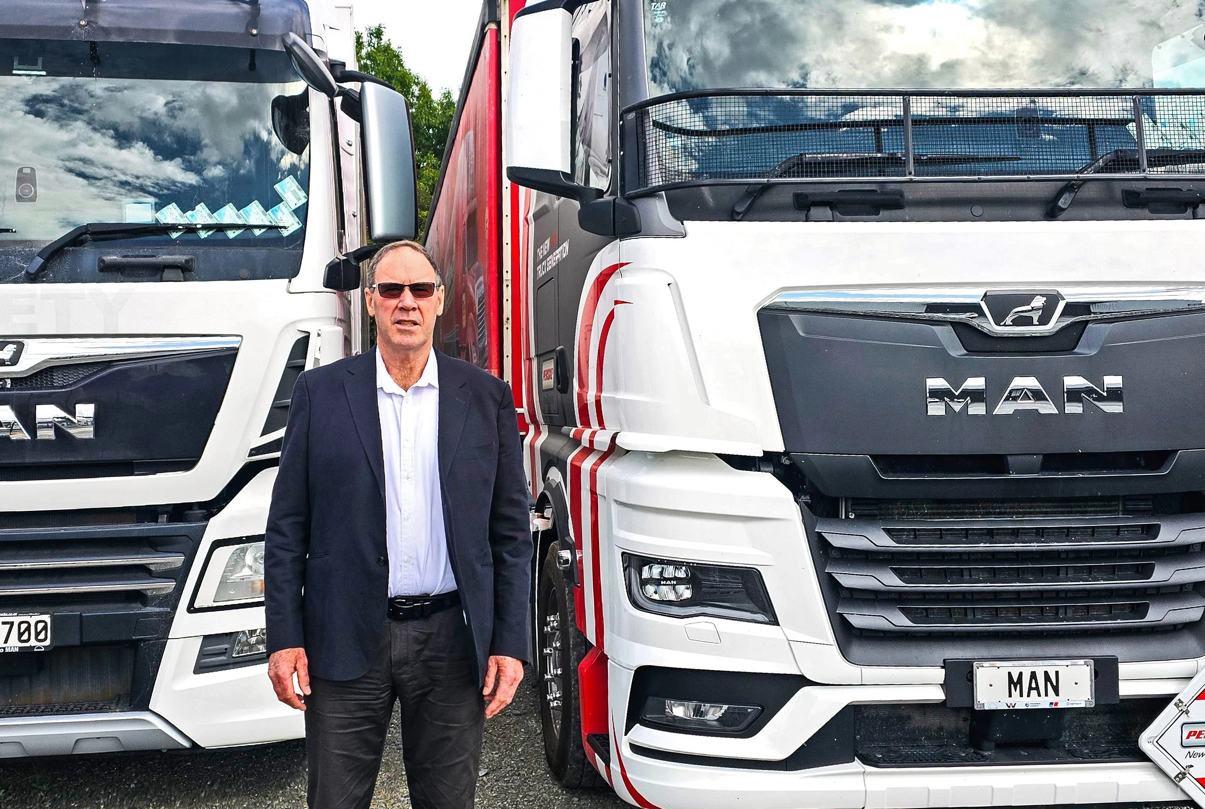 A man stading in front of two trucks, one white, one white with red and black stripes