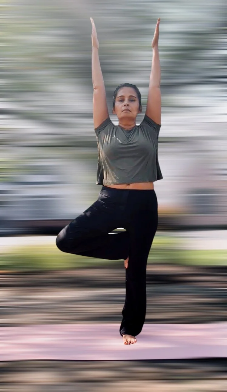 Woman practicing yoga outdoors in tree pose on yoga mat.