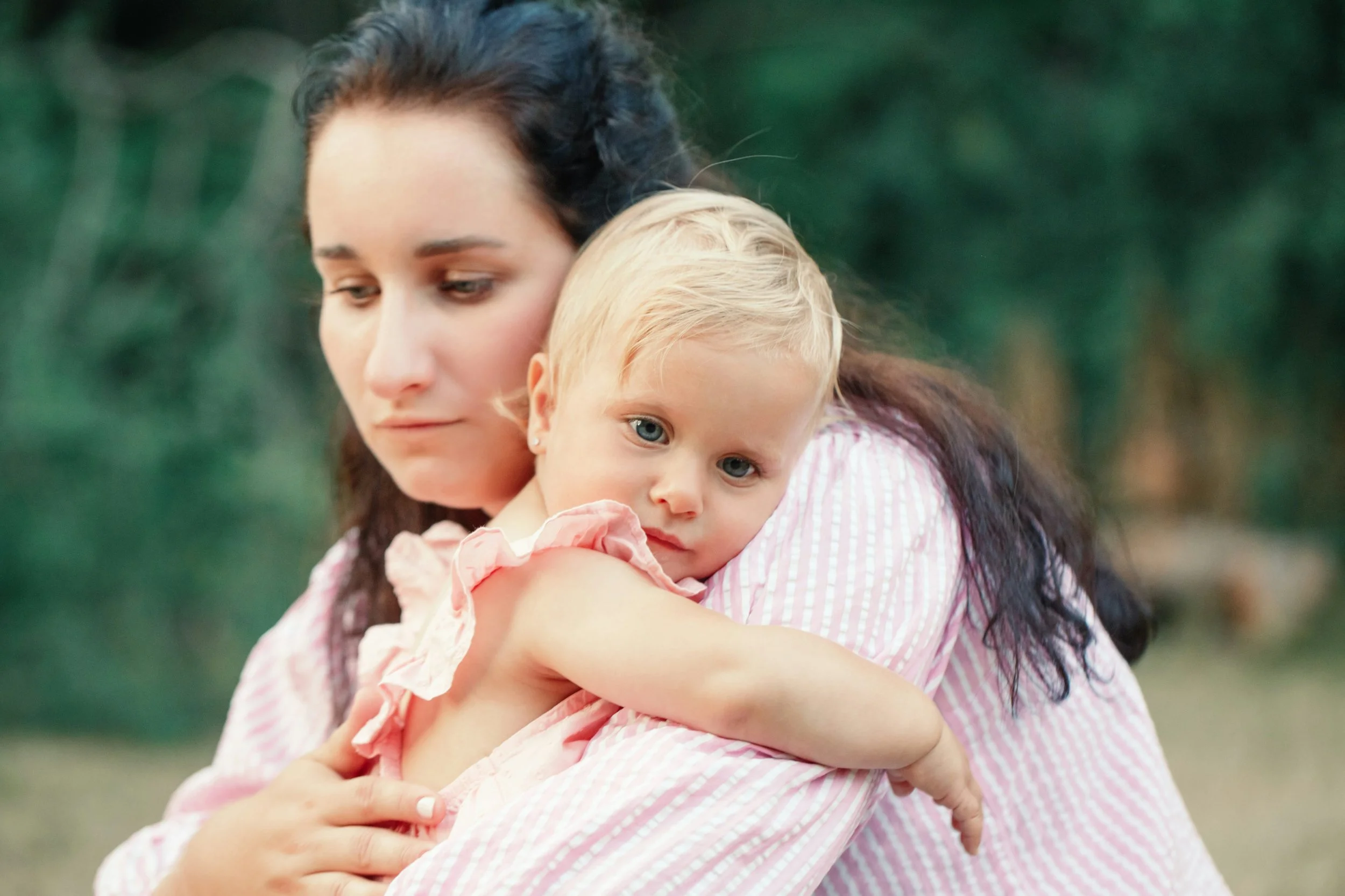 Mother holding her young daughter with a tired, faraway expression, illustrating the invisible mental load of motherhood