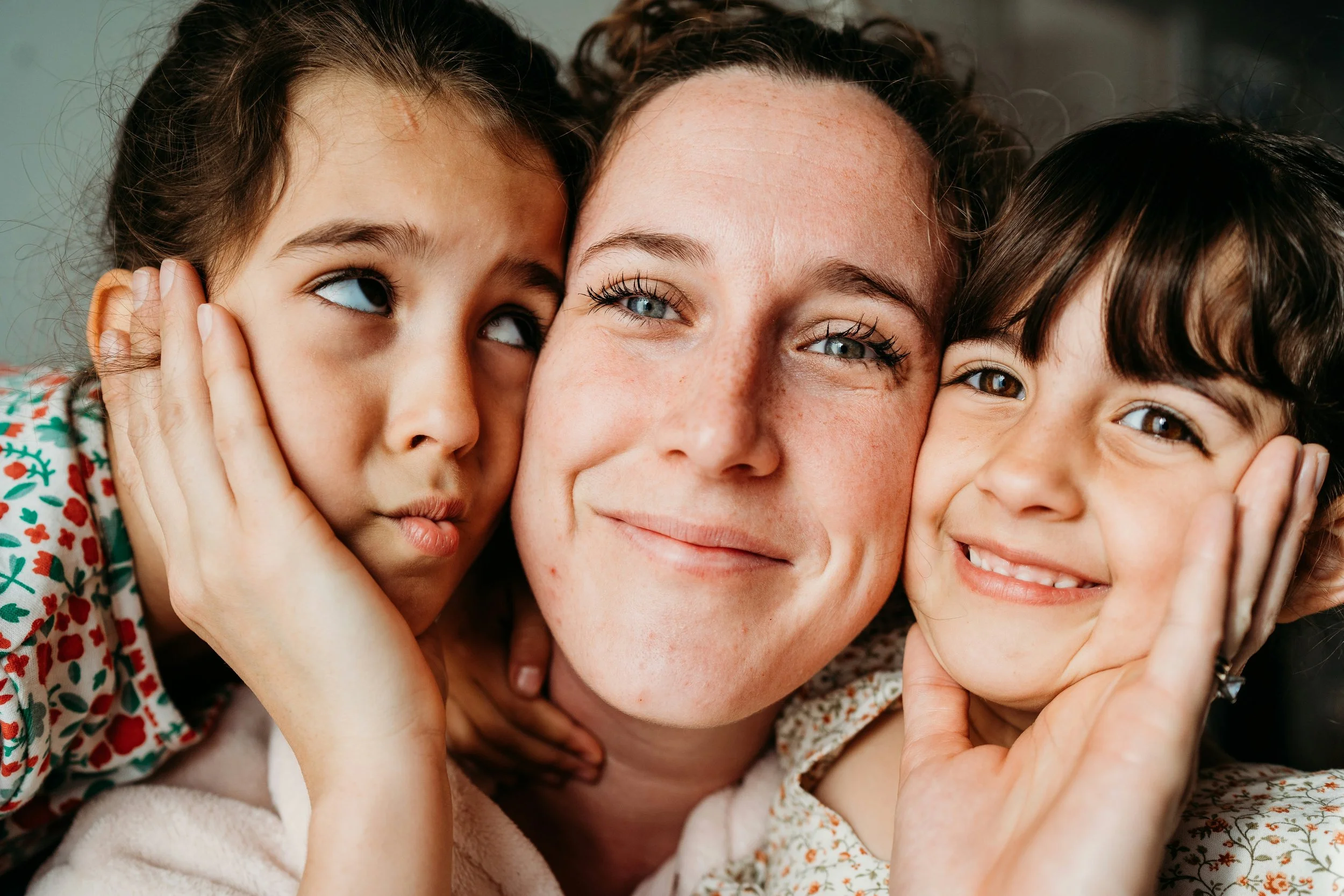 Mother resting cheek to cheek with her two young daughters, all three faces close together