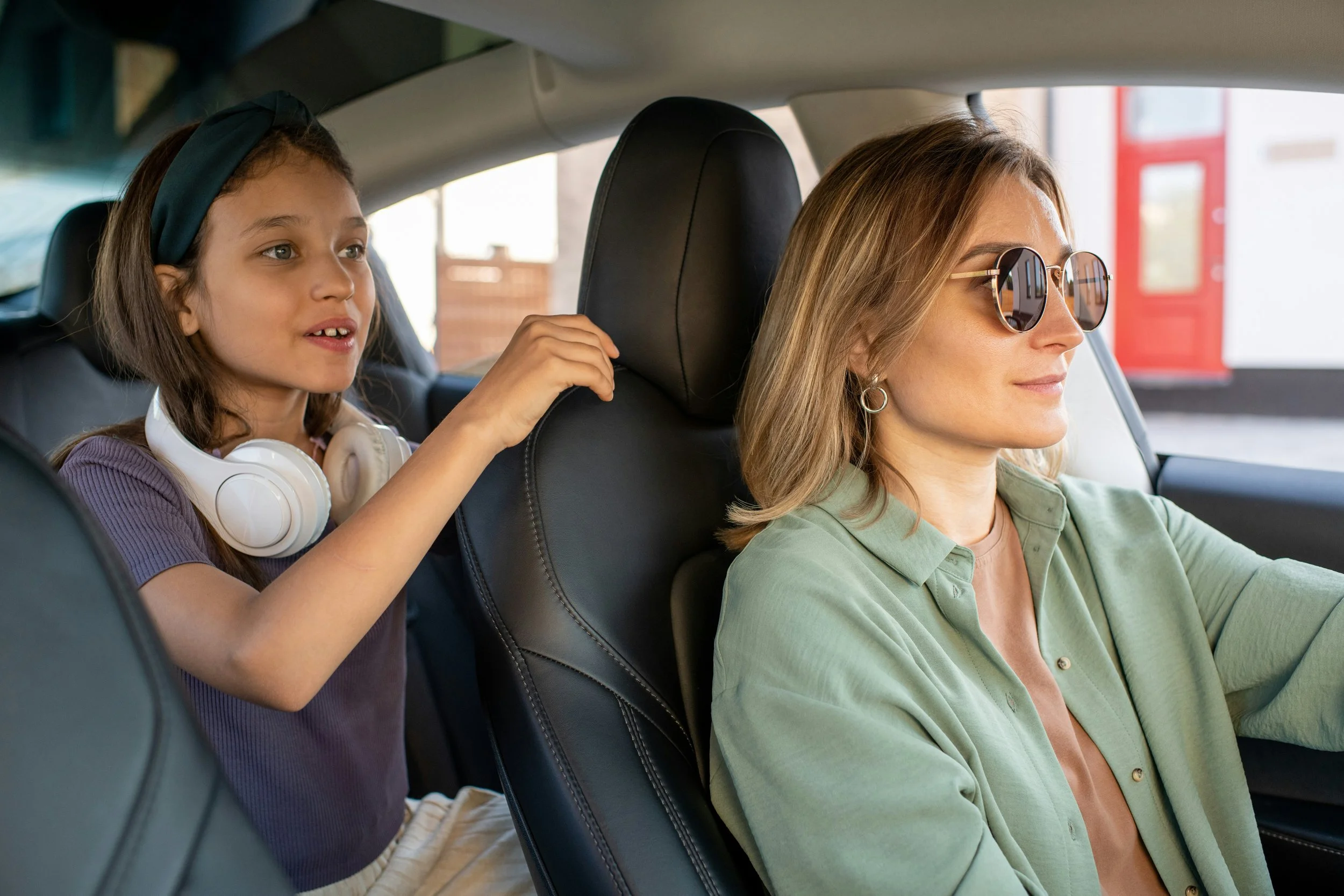 Mom driving while her daughter leans forward from the back seat mid-story after school pickup