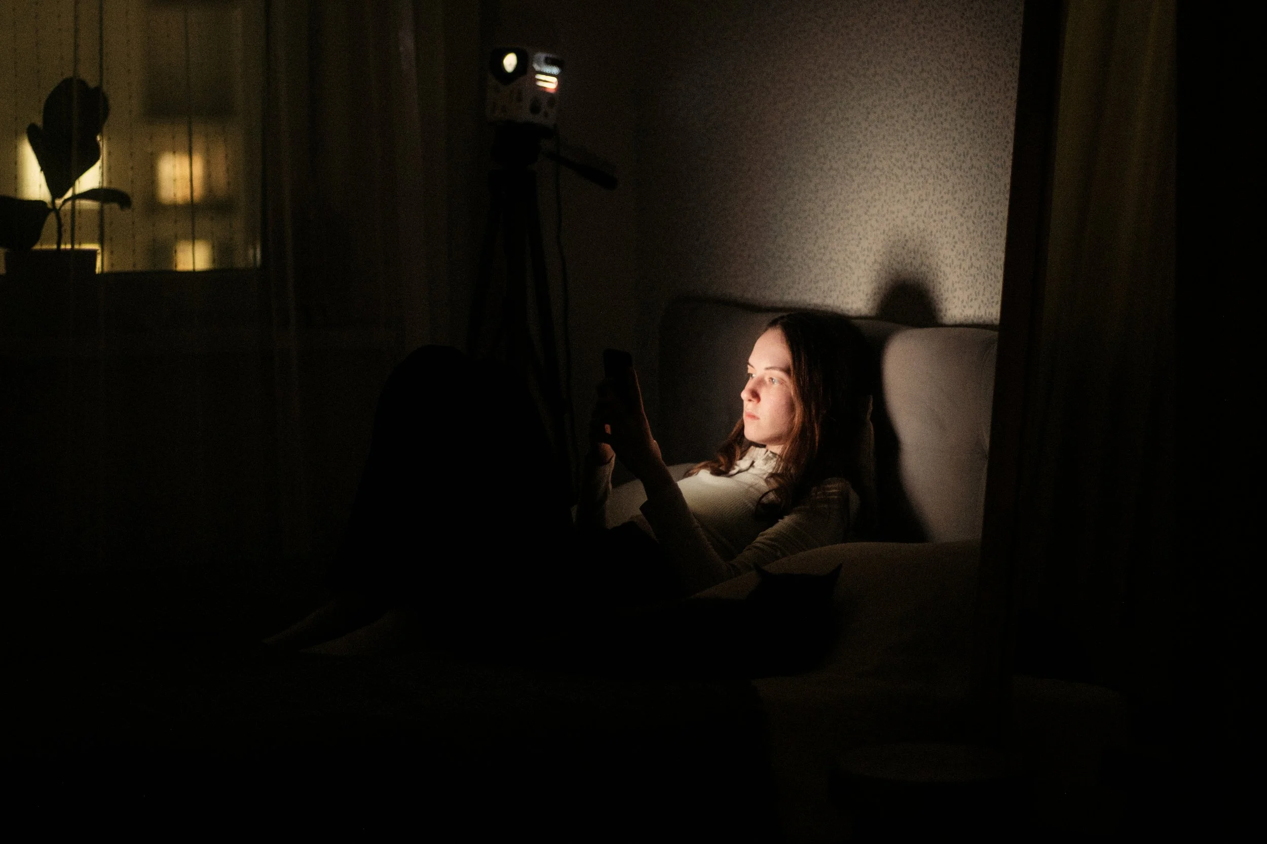 A woman lying on a couch in a dark room, her face lit by her phone screen