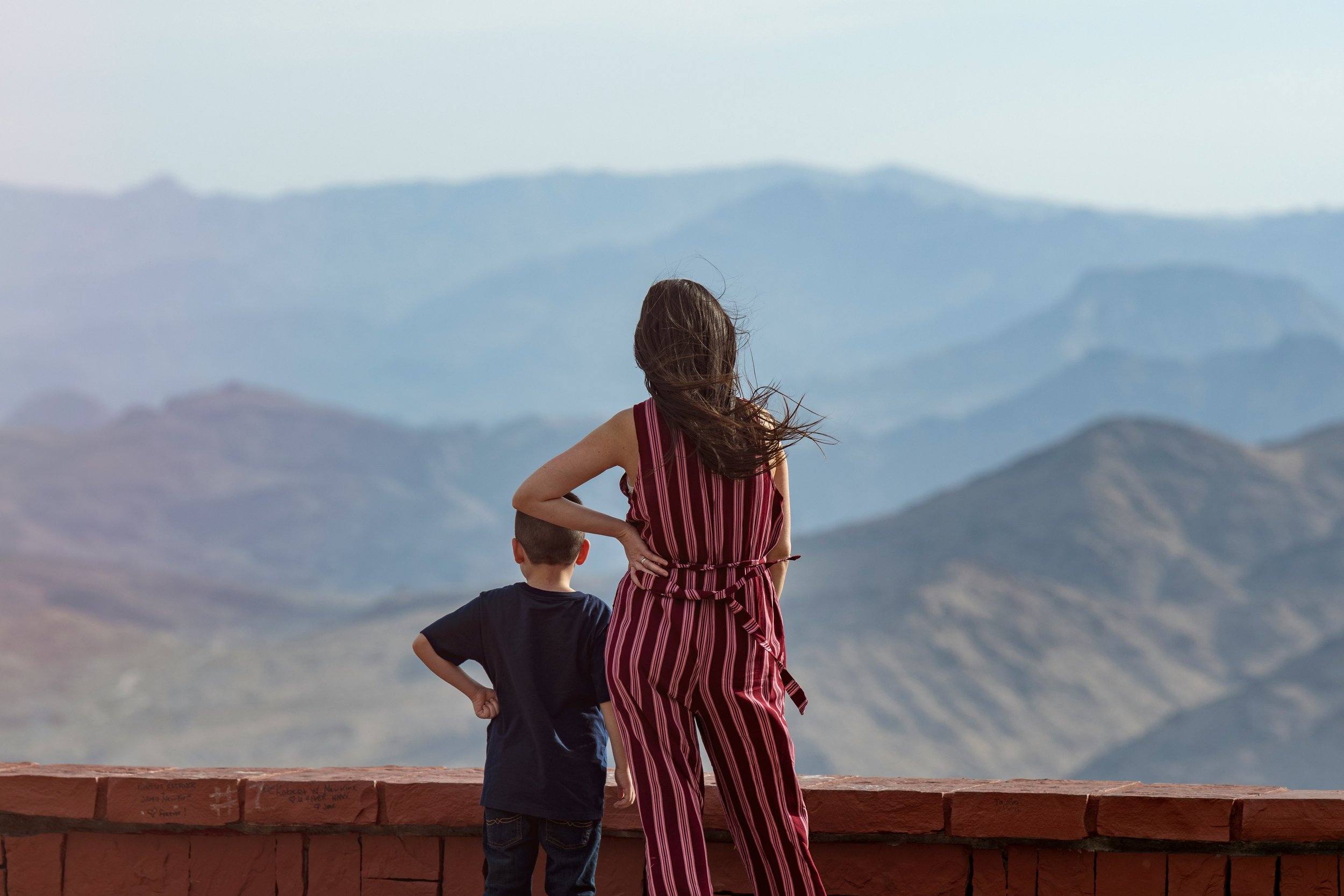 A mother and young child standing side by side looking out at a mountain landscape