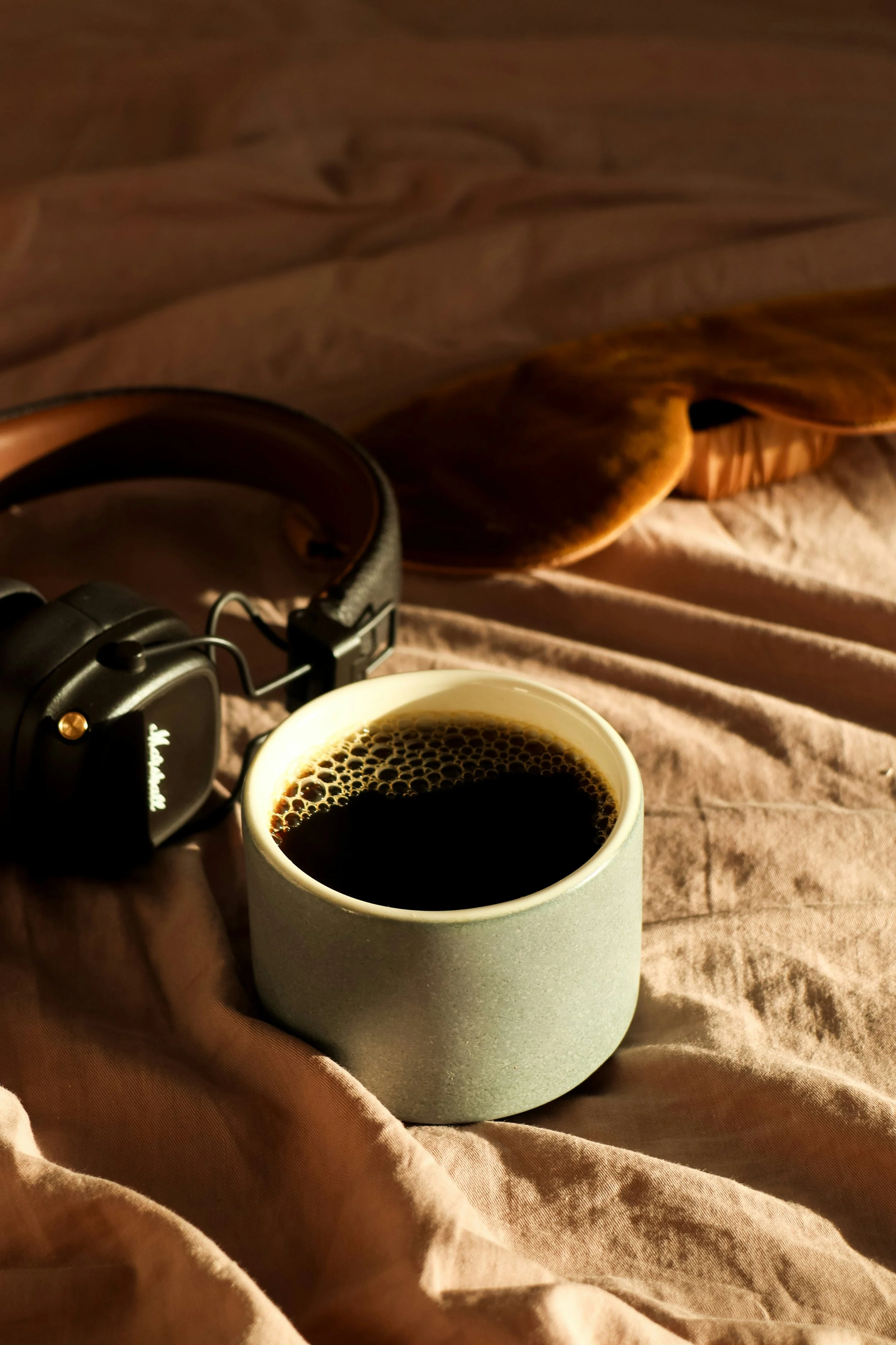 Noise-cancelling headphones and a cup of coffee on a bed, tools for reducing sensory input during overstimulation.