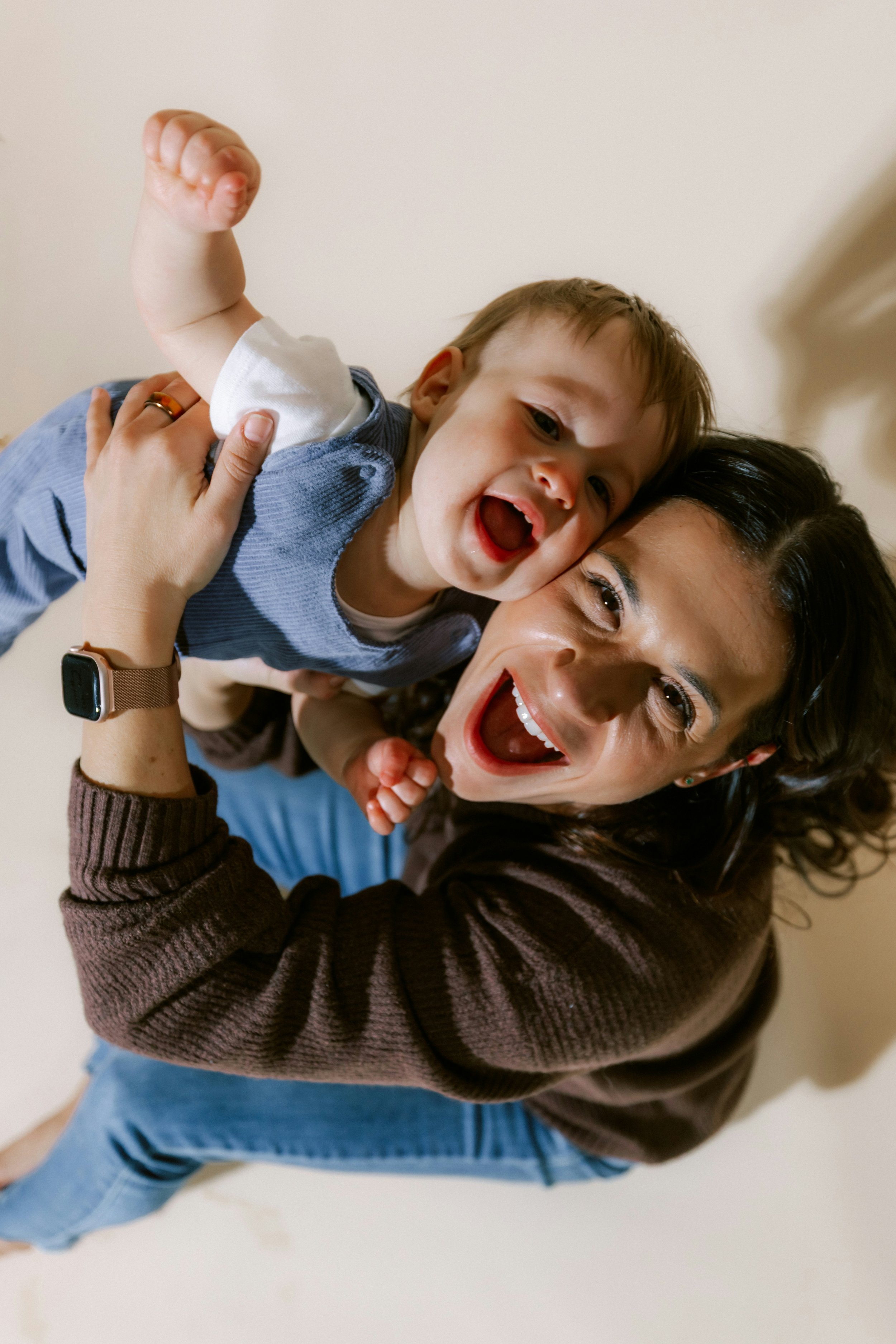 Smiling mother lifting her laughing baby overhead against a warm neutral background