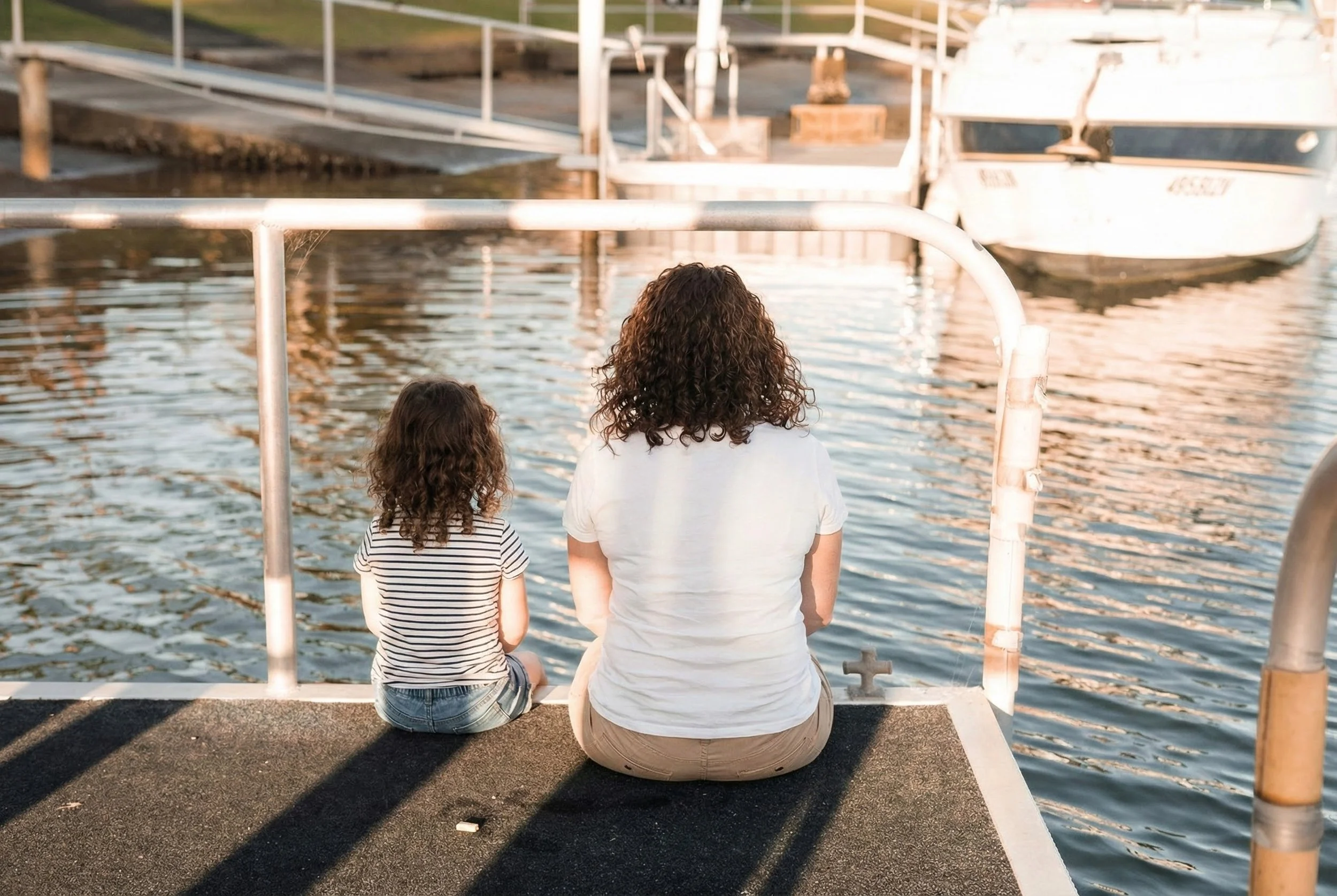 A woman and child sitting together on a pier looking at the water in golden light. A visual representation of breaking cycles, mother-daughter connection, and offering presence after an emotional rupture.