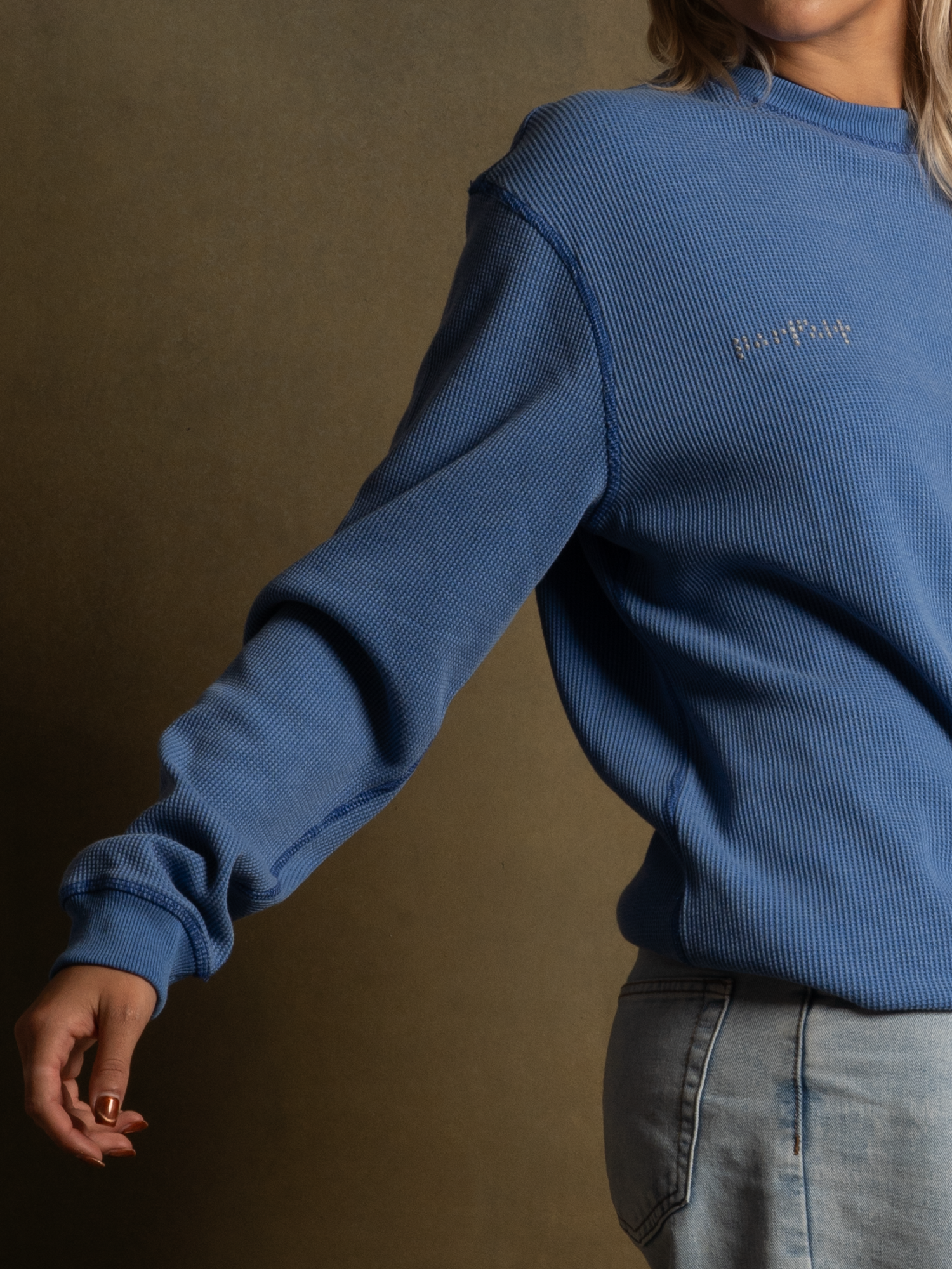 Close-up of a woman wearing a blue long-sleeve athletic top with small embroidered text on the chest and light denim jeans.