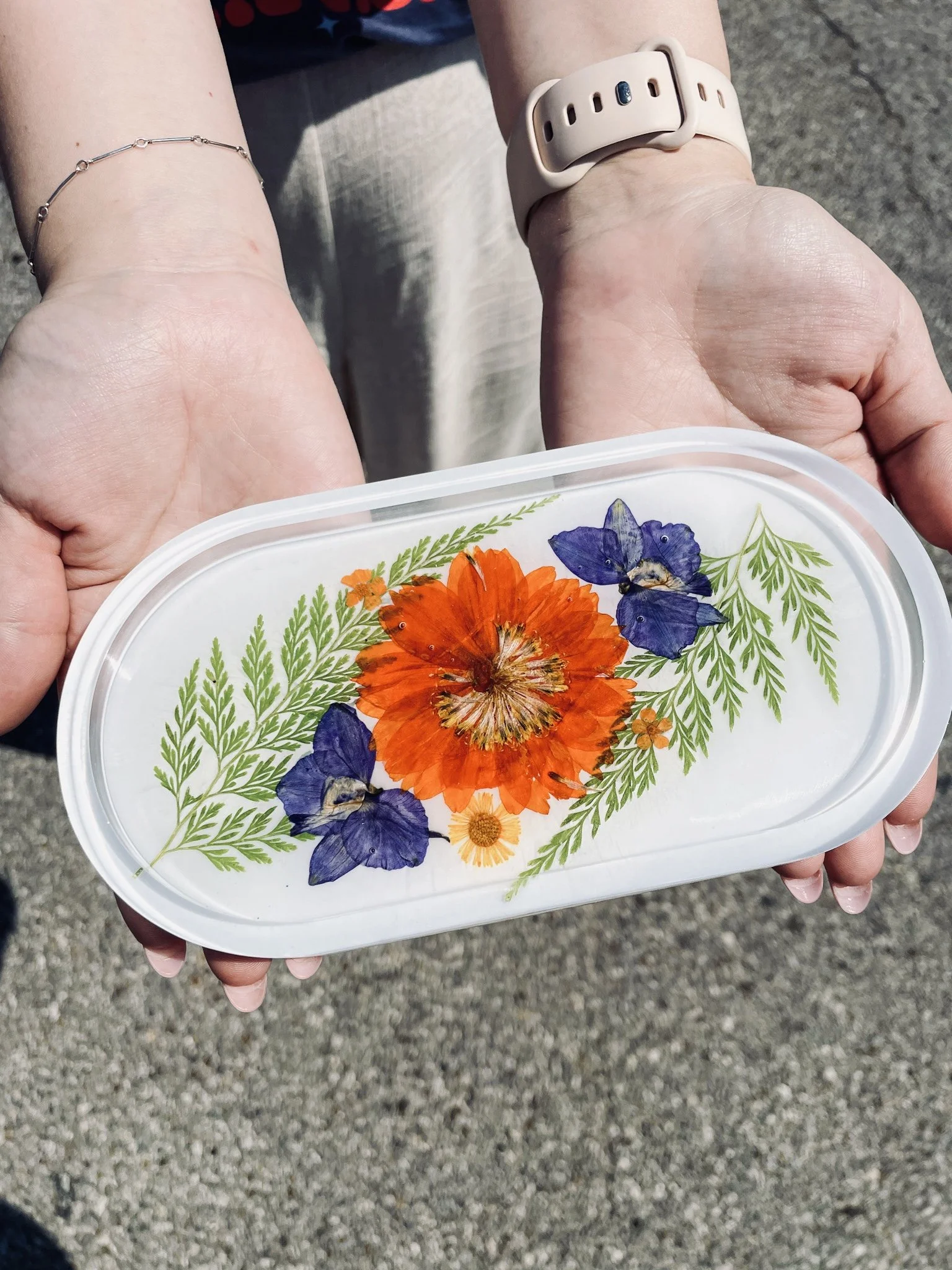 Hands hold a catch-all try with orange and blue focal flowers with greenery