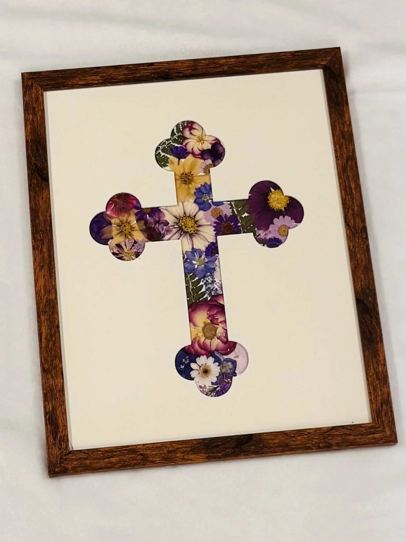 A framed cross made out of purple, yellow, and white pressed flowers