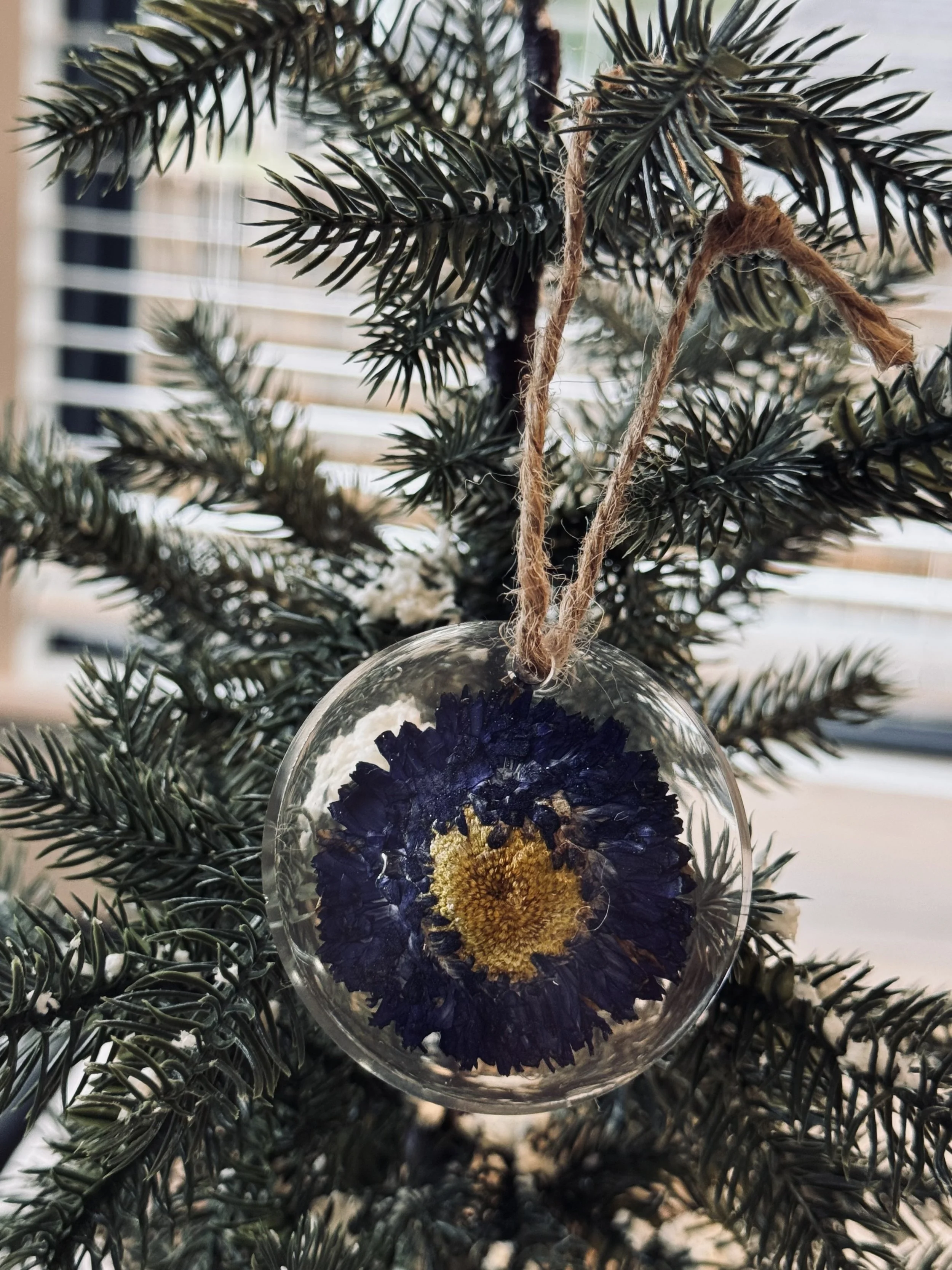 A resin ornament with a purple flower hangs on a Christmas tree