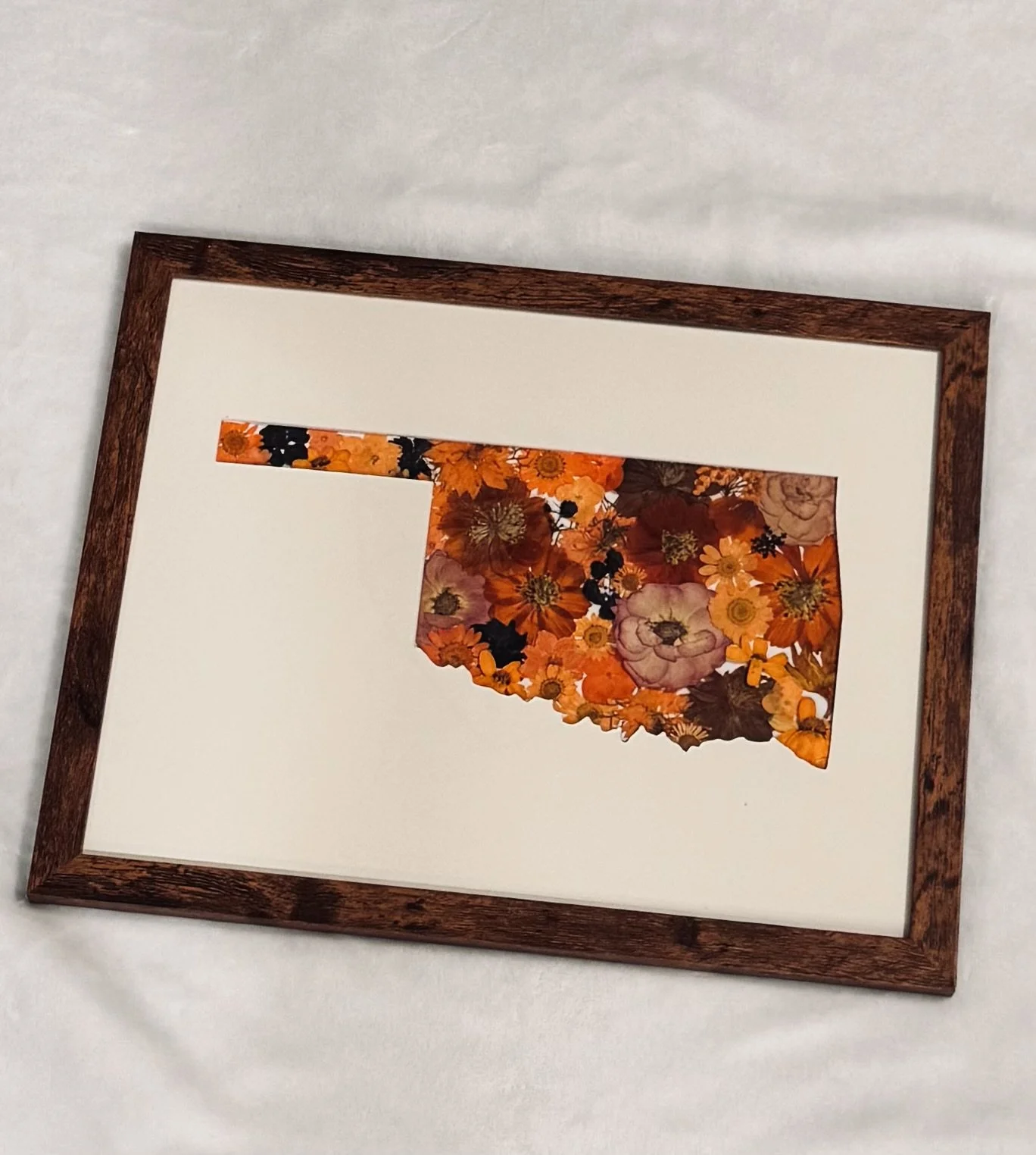 A framed silhouette of Oklahoma with orange flowers with black floral details