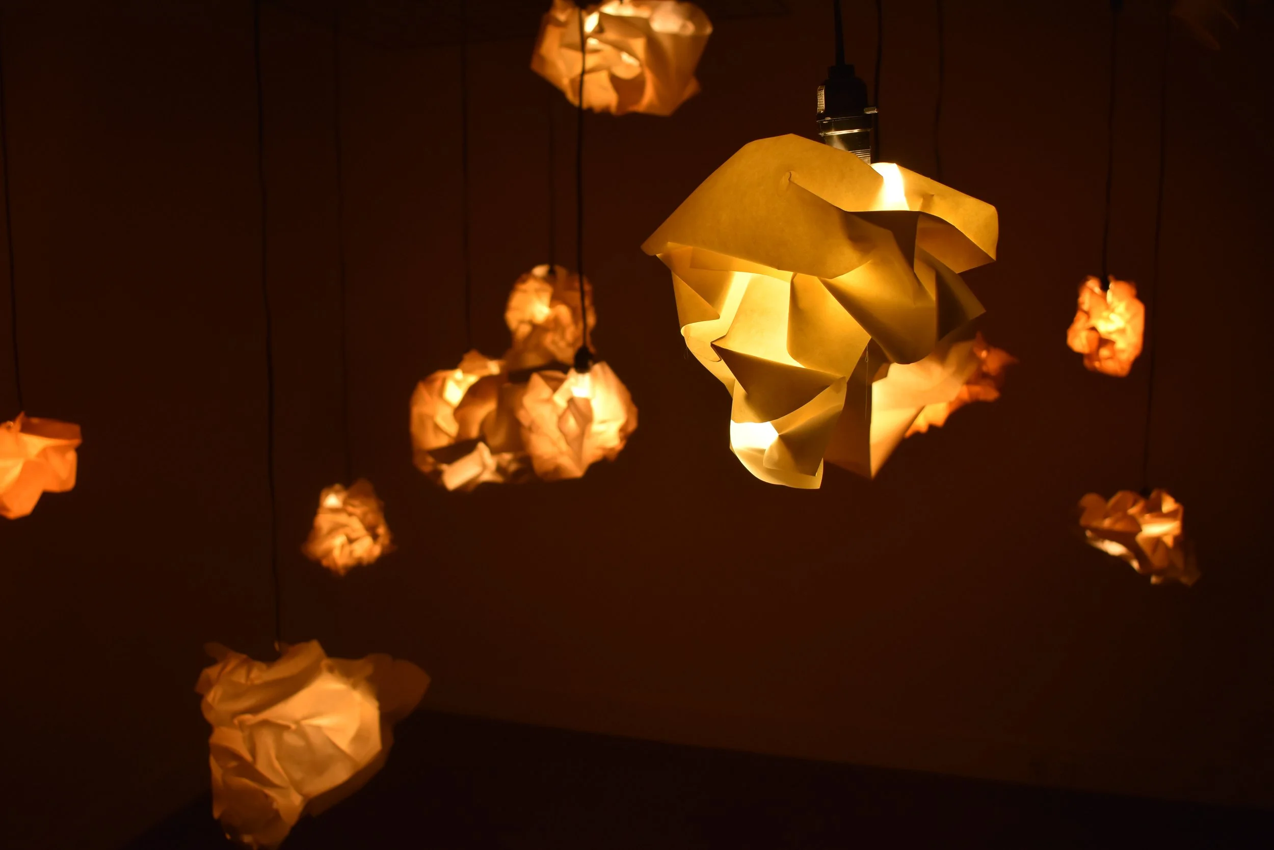 Hanging paper lanterns in various shapes emitting a warm yellow light against a dark background.