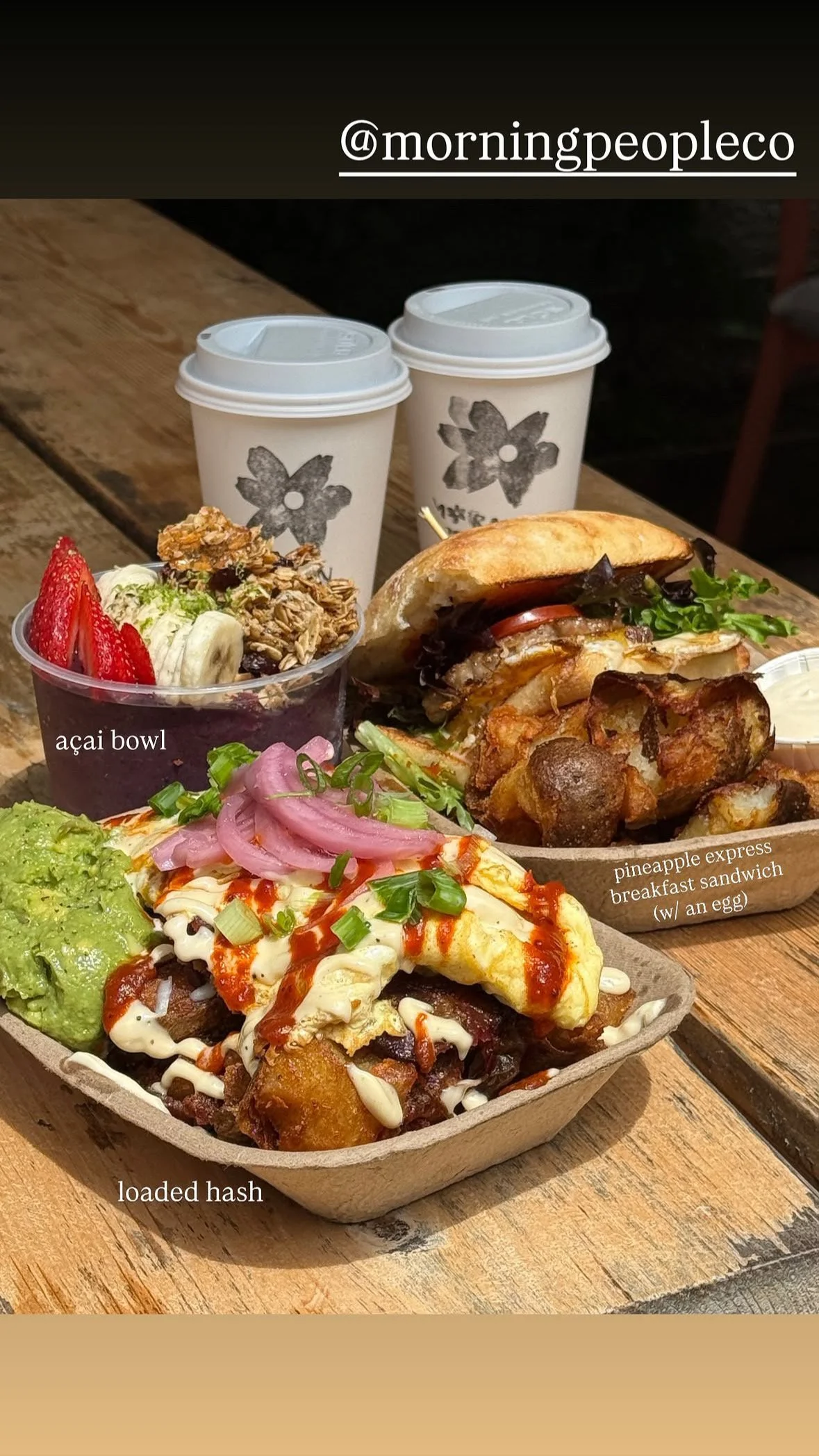 A meal consisting of a loaded hash with avocado, eggs, and sauce, a pineapple express breakfast sandwich with an egg, local oyster mushrooms, and vegetables, an acai bowl with strawberries, granola, and banana, and two cups of coffee.