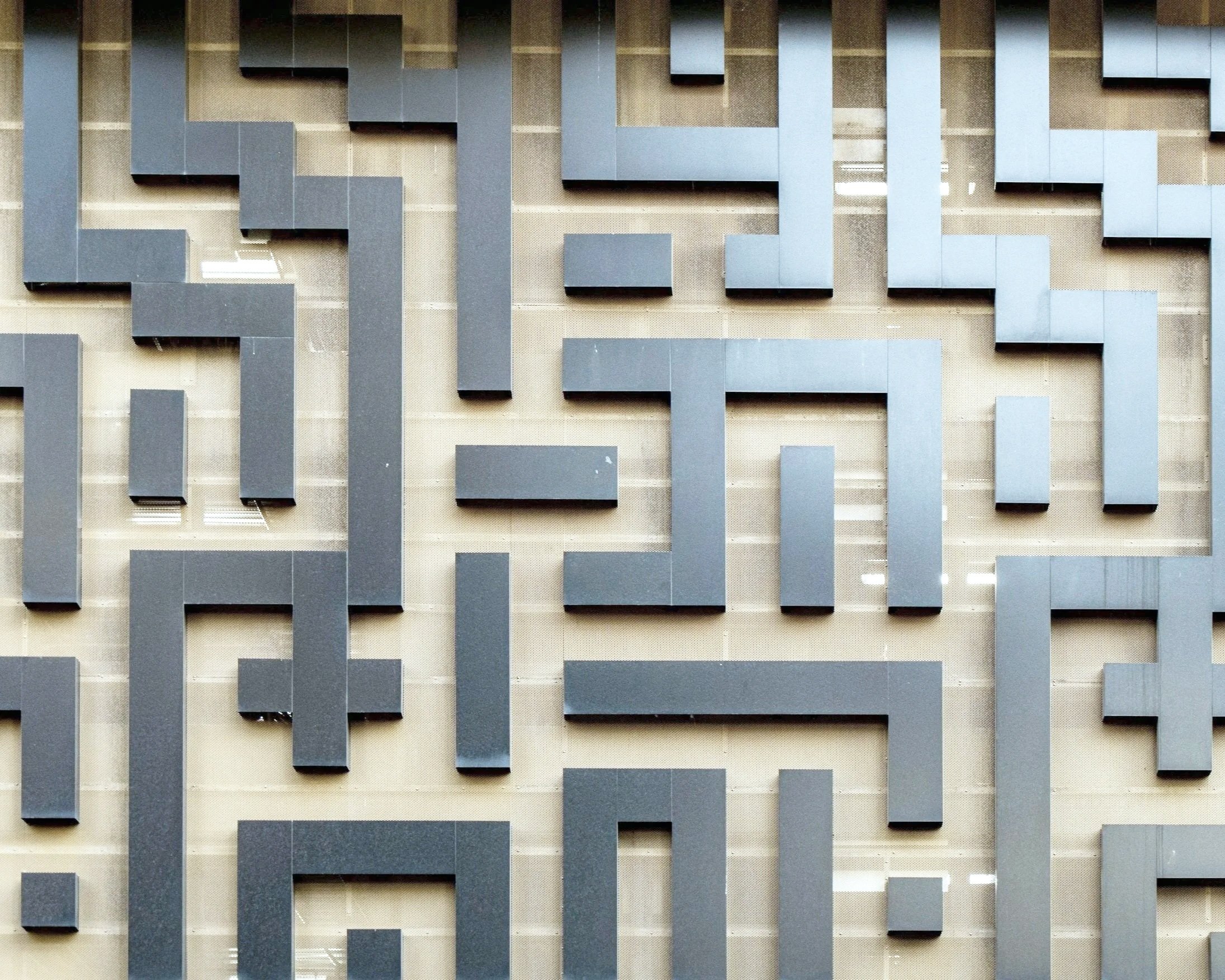 Close-up of a beige wall with a maze-like pattern of dark gray three-dimensional rectangular elements.