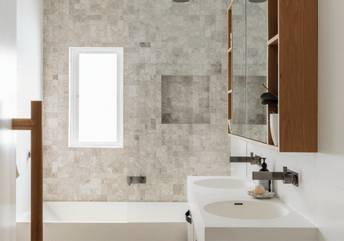 Modern bathroom with a white sink, a wooden storage cabinet with shelves, a large mirror, a small window, and a tiled shower area with a square niche for toiletries.