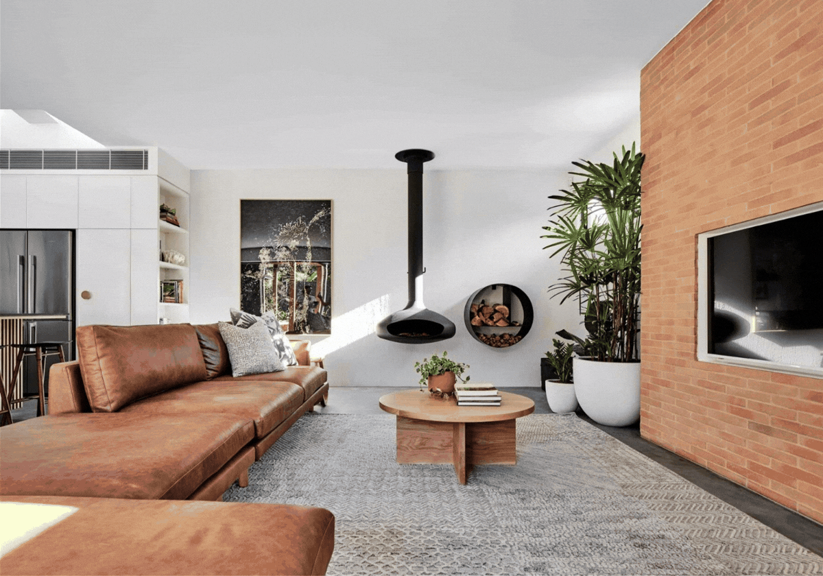 Modern living room with leather sofa, coffee table, fireplace, TV, and large potted plants.