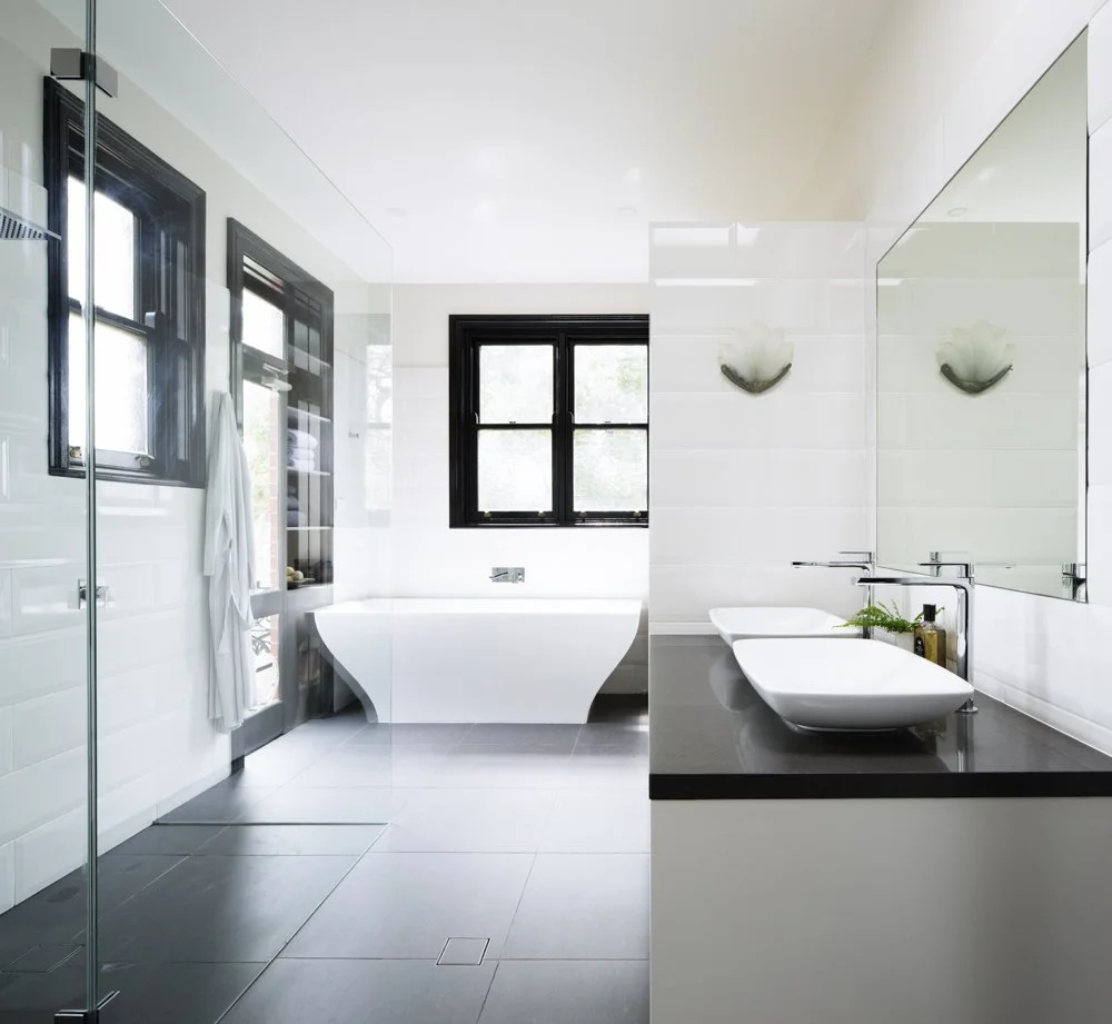 Modern bathroom with white walls, black-framed windows, a freestanding bathtub, a vessel sink on a black countertop, large mirror, and minimal decor.