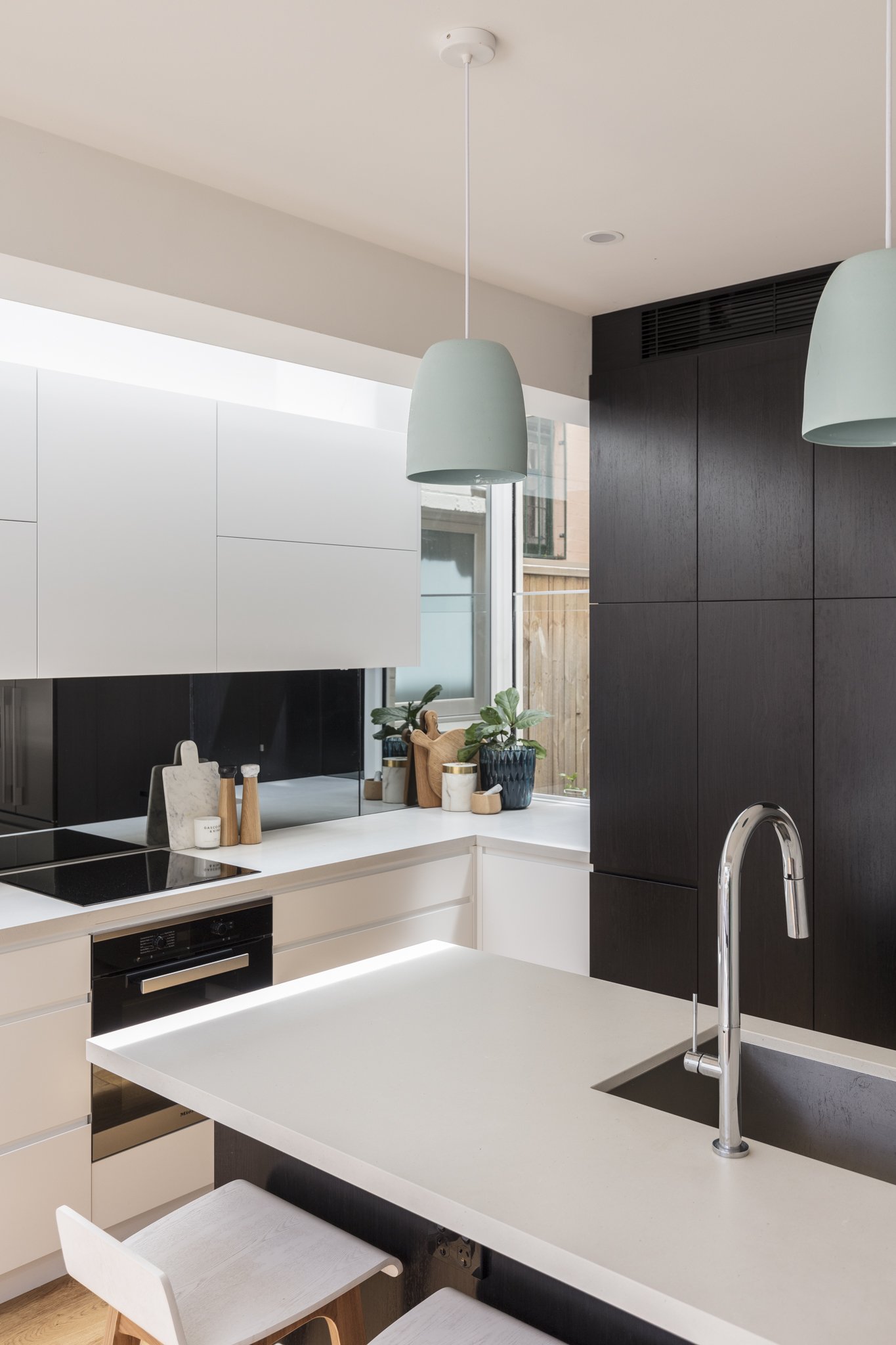 Modern kitchen with white countertops, dark wood cabinets, pendant lights, and plants near a window.