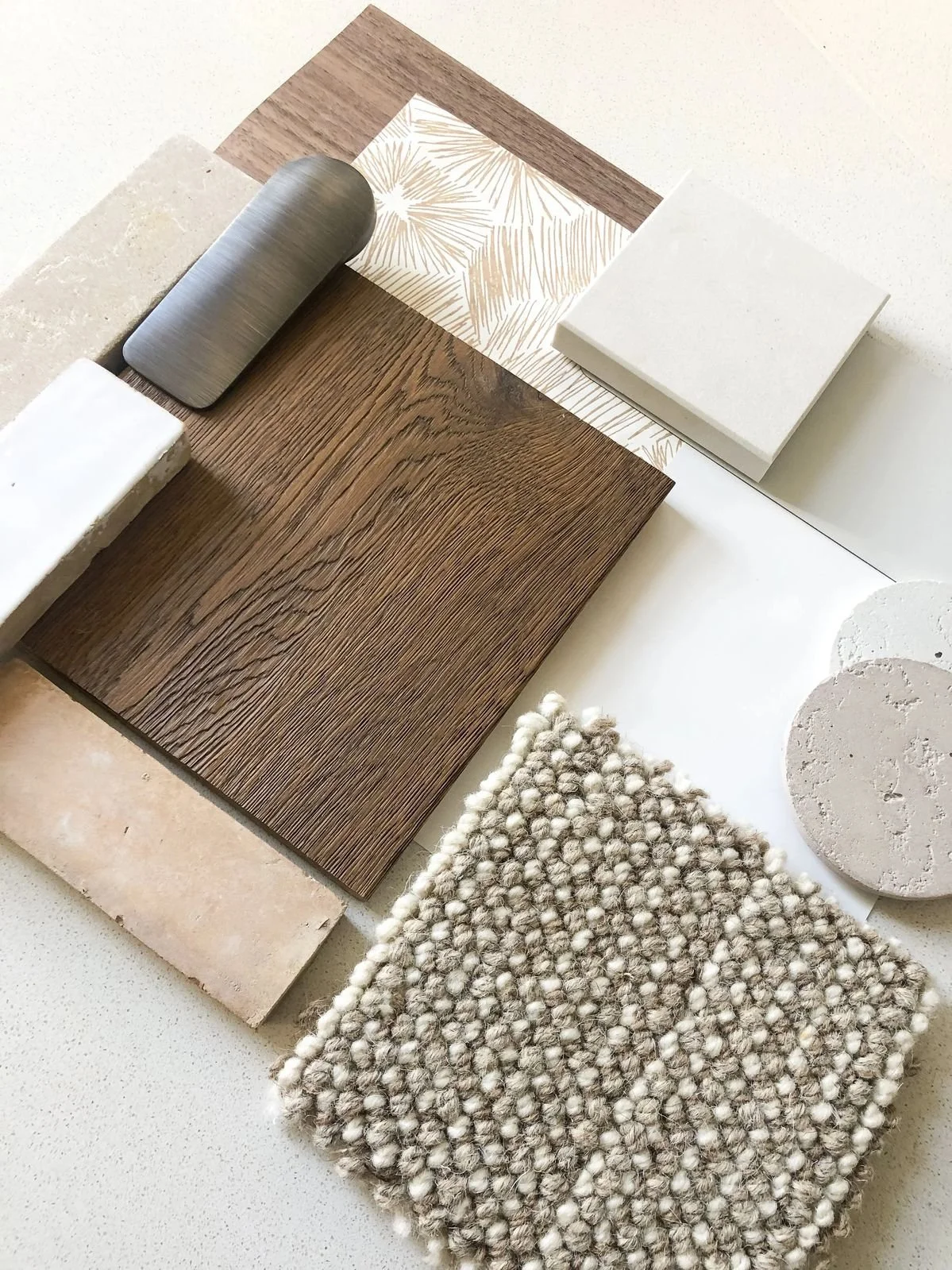 Arrangement of various material samples including wood, tile, fabric, stone, and carpet in neutral tones.