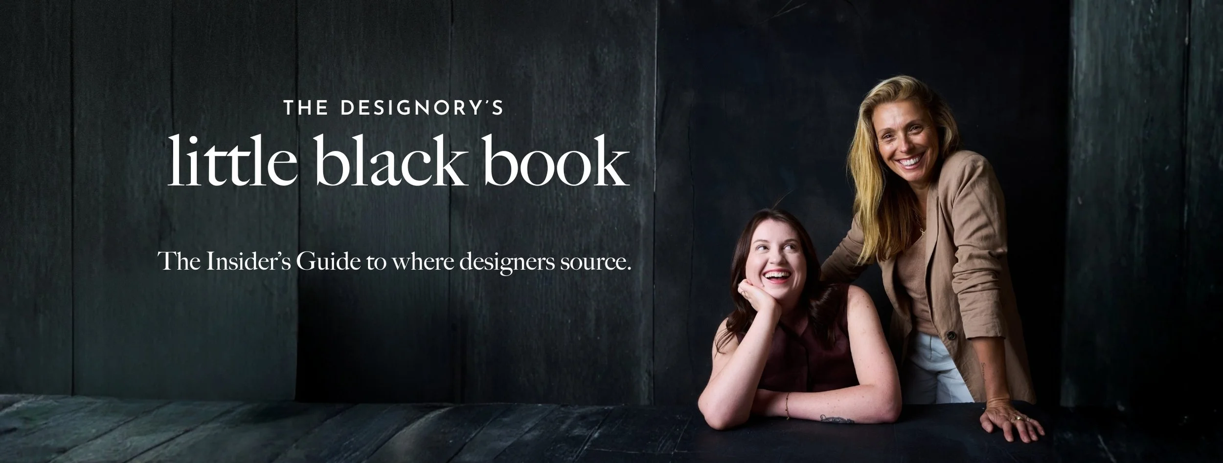 Two women smiling, one seated and one standing, in front of dark wooden panels. The text overlays say "The designory's little black book" and "The insider's guide to where designers source."