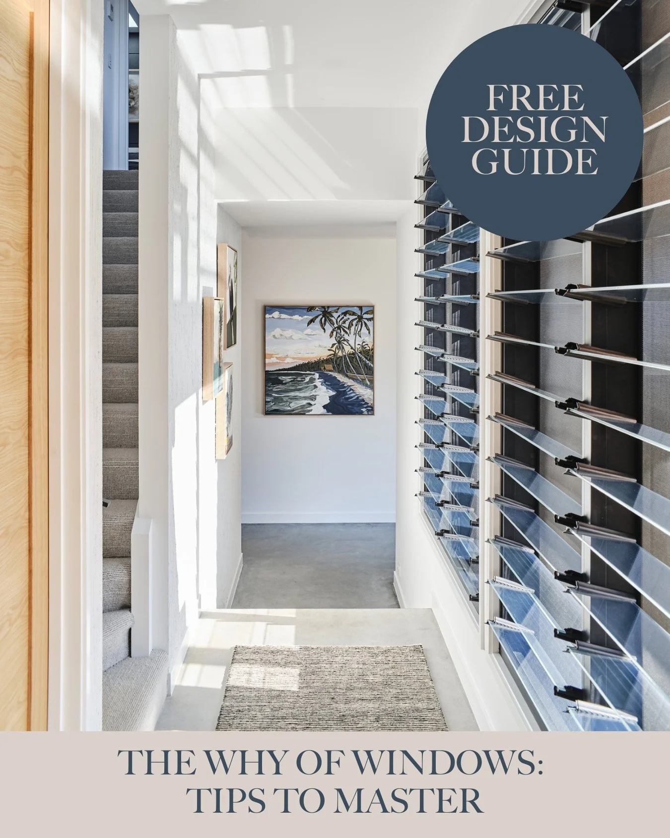 A narrow entryway with white walls, featuring a framed landscape painting of a beach scene with palm trees, set between shelves of mail slots or small storage compartments on the right. Sunlight casts shadows on the left wall near a staircase.