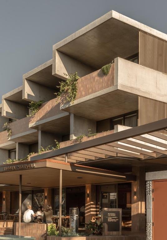 Exterior view of Hotel Marvel featuring modern concrete balconies with greenery and a ground-floor outdoor seating area with people dining.
