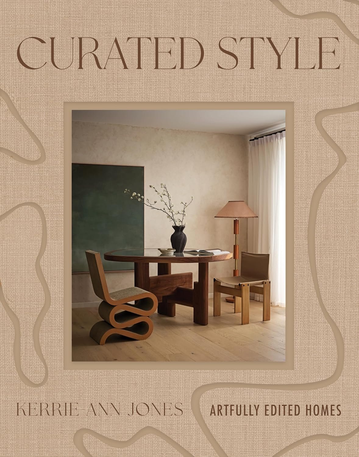 Book cover titled 'Curated Style' by Kerrie Ann Jones featuring a photo of a minimalist dining room with a wooden round table, two chairs, a vase with branches, and a floor lamp.