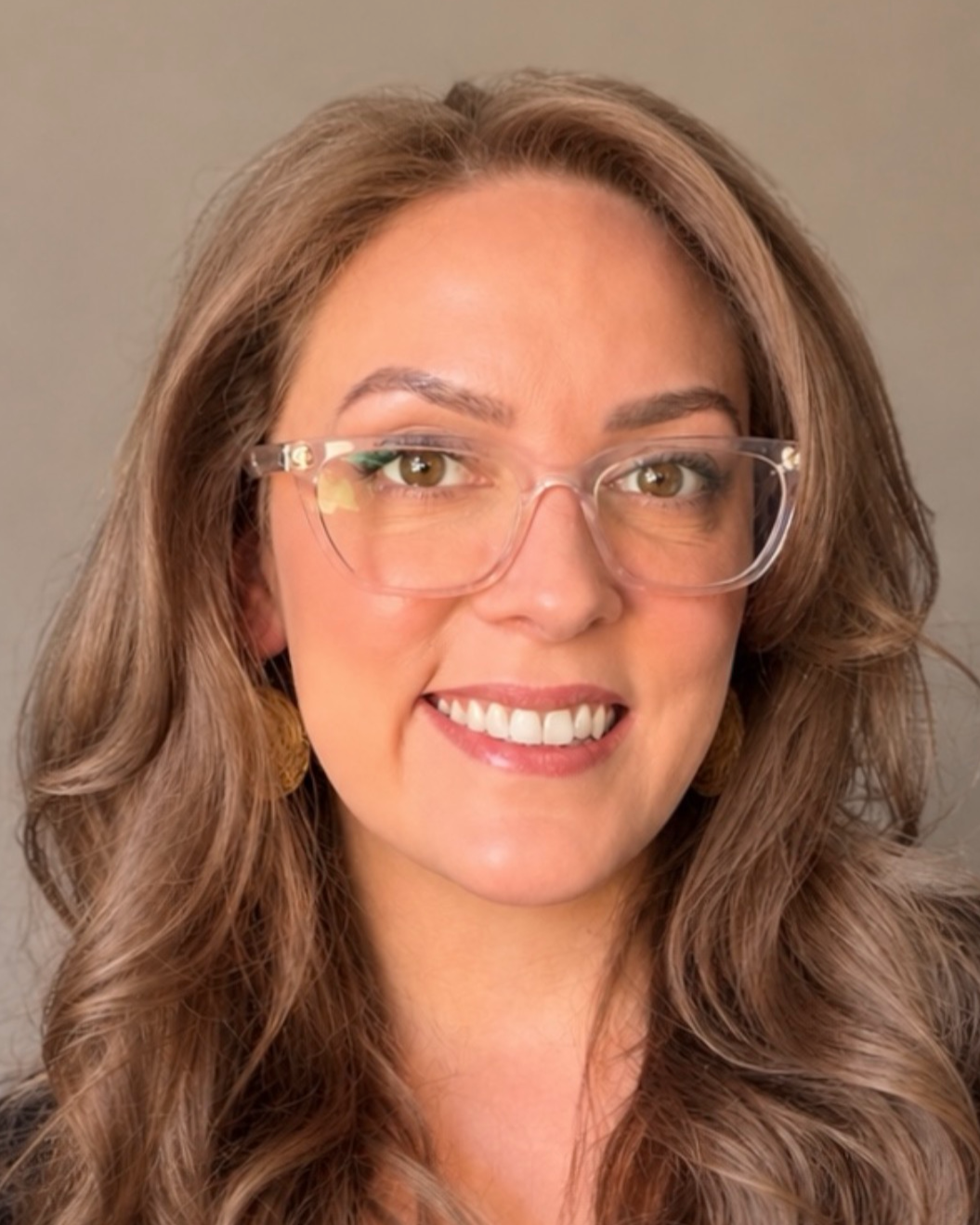 Close-up of a woman with brown wavy hair wearing glasses and smiling at the camera.