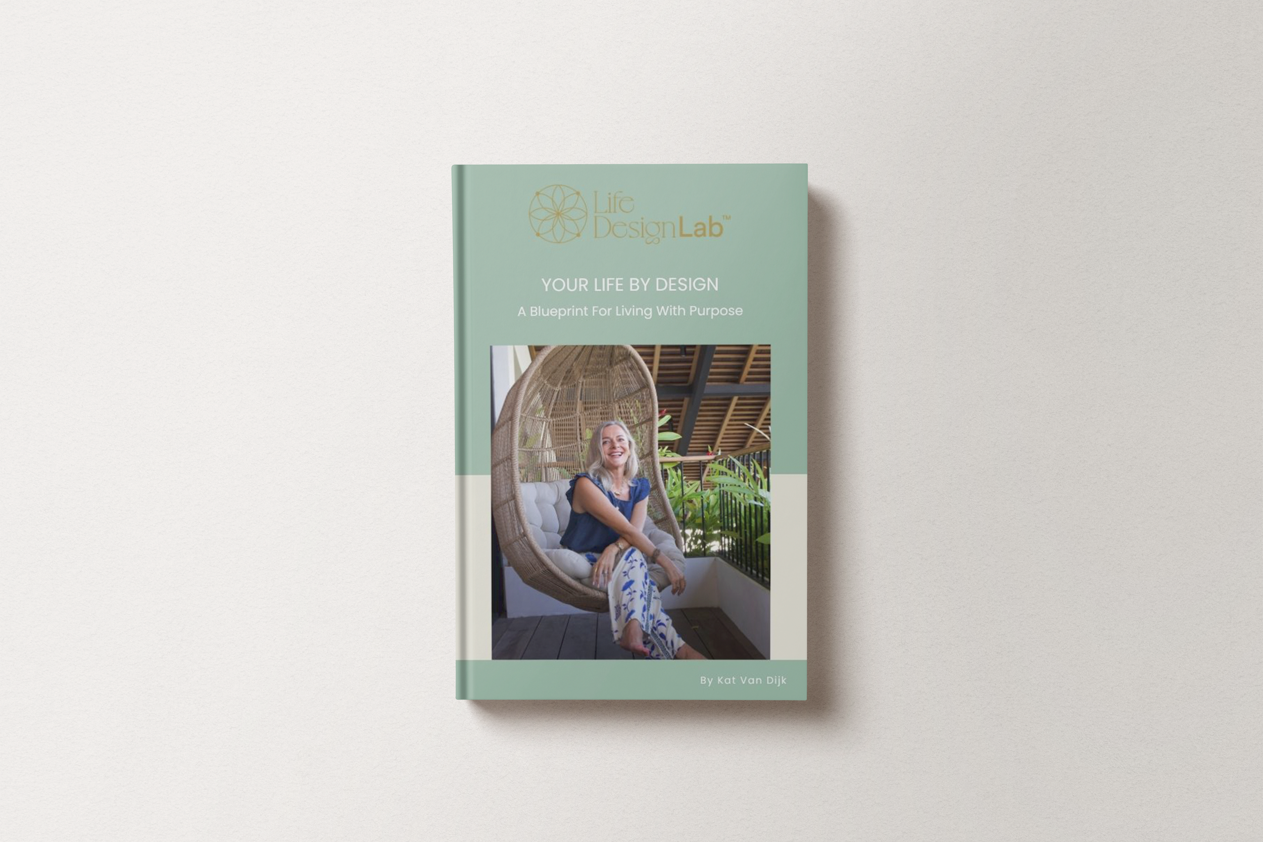 A book titled "Your Life by Design: A Blueprint For Living With Purpose" by Kat Van Dijk, featuring a cover image of a smiling woman sitting in a wicker hanging chair on a balcony with green plants and a wooden roof.