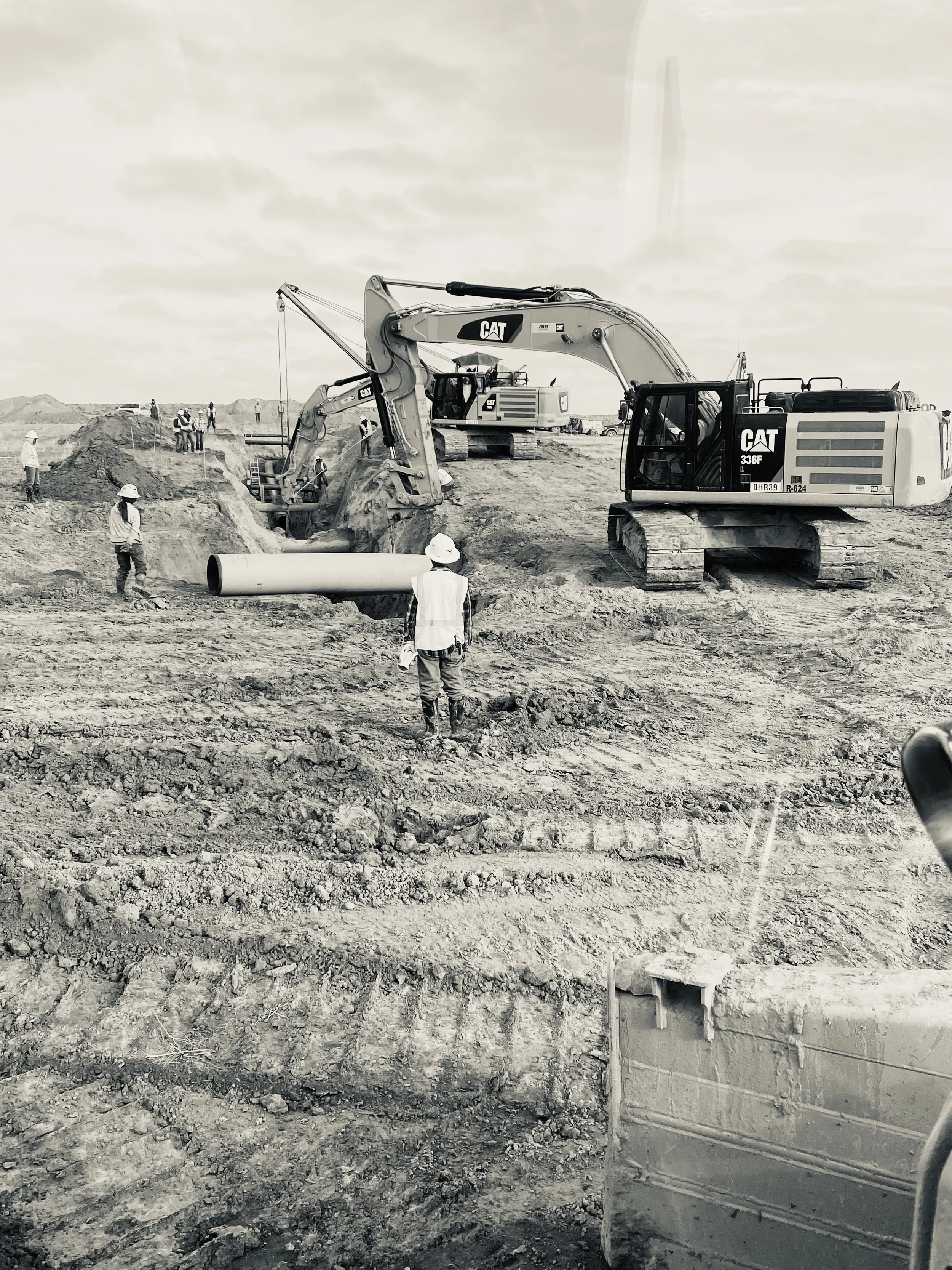 Construction site with workers and heavy machinery, including excavators and pipes, working on earth and soil.