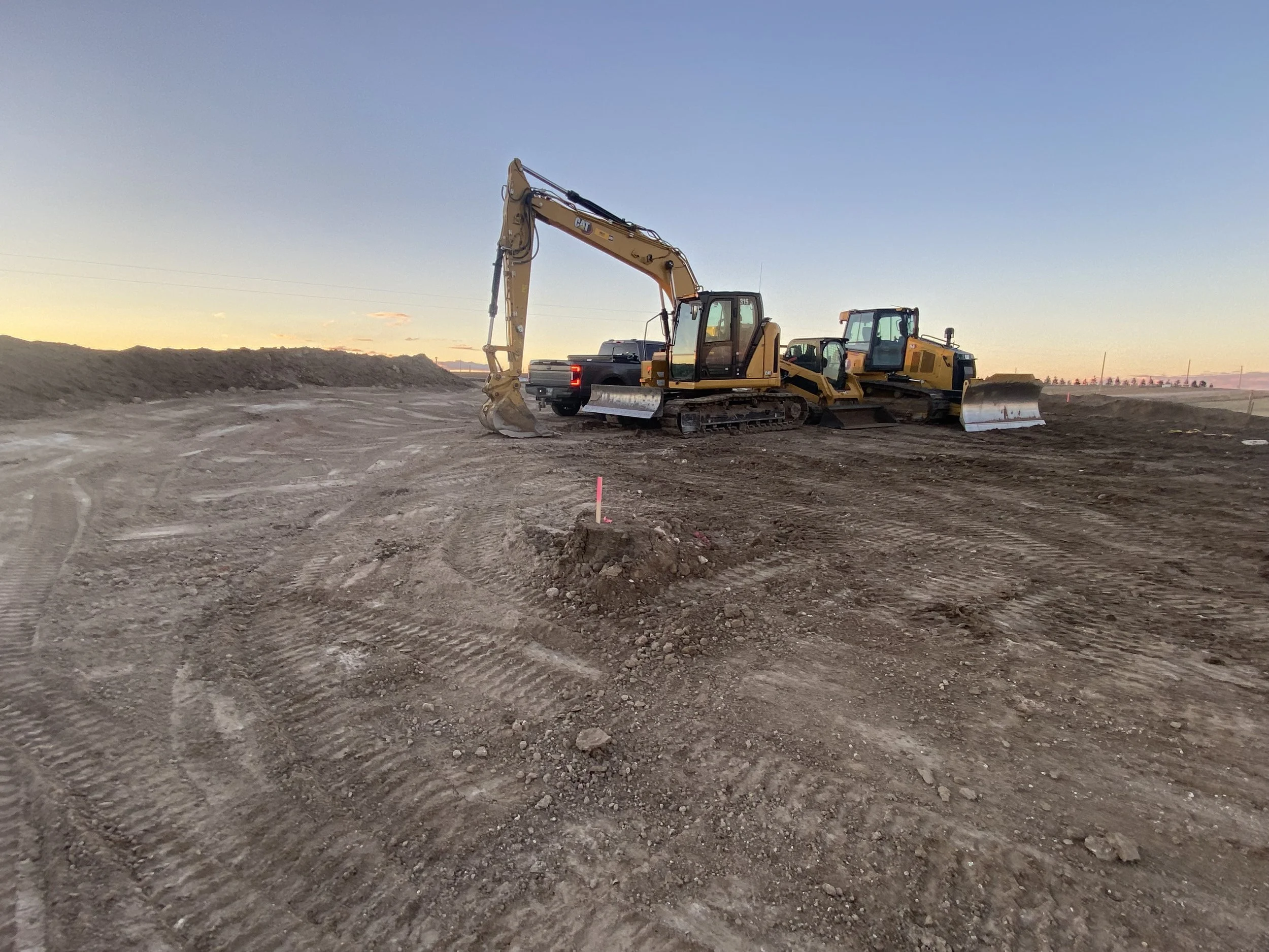 Construction site at sunset with a yellow excavator and a bulldozer on dirt ground.