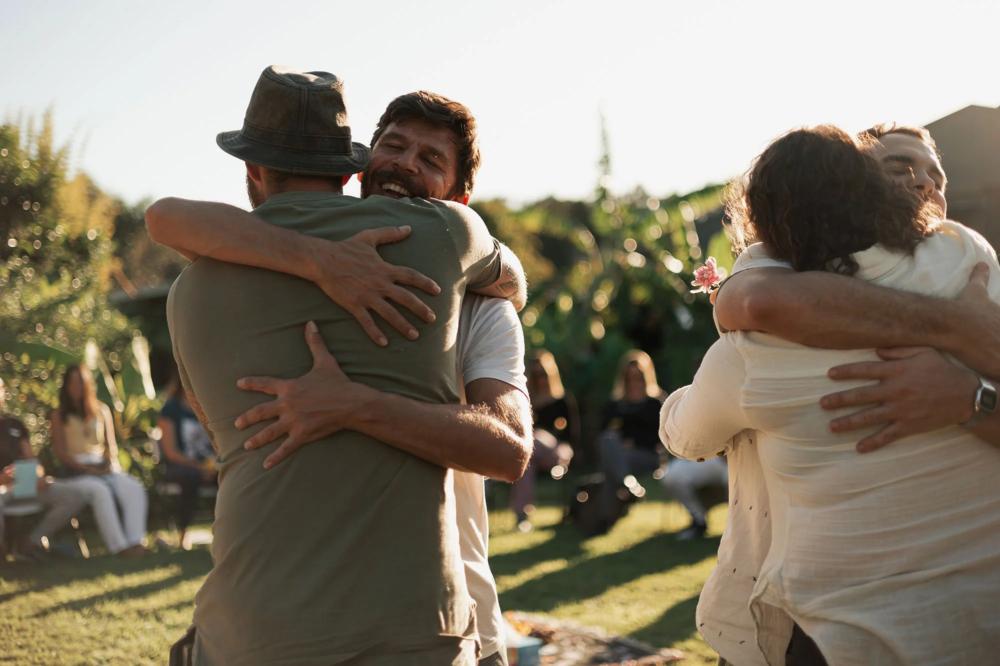 People hugging outdoors, some sitting in the background, during daytime.